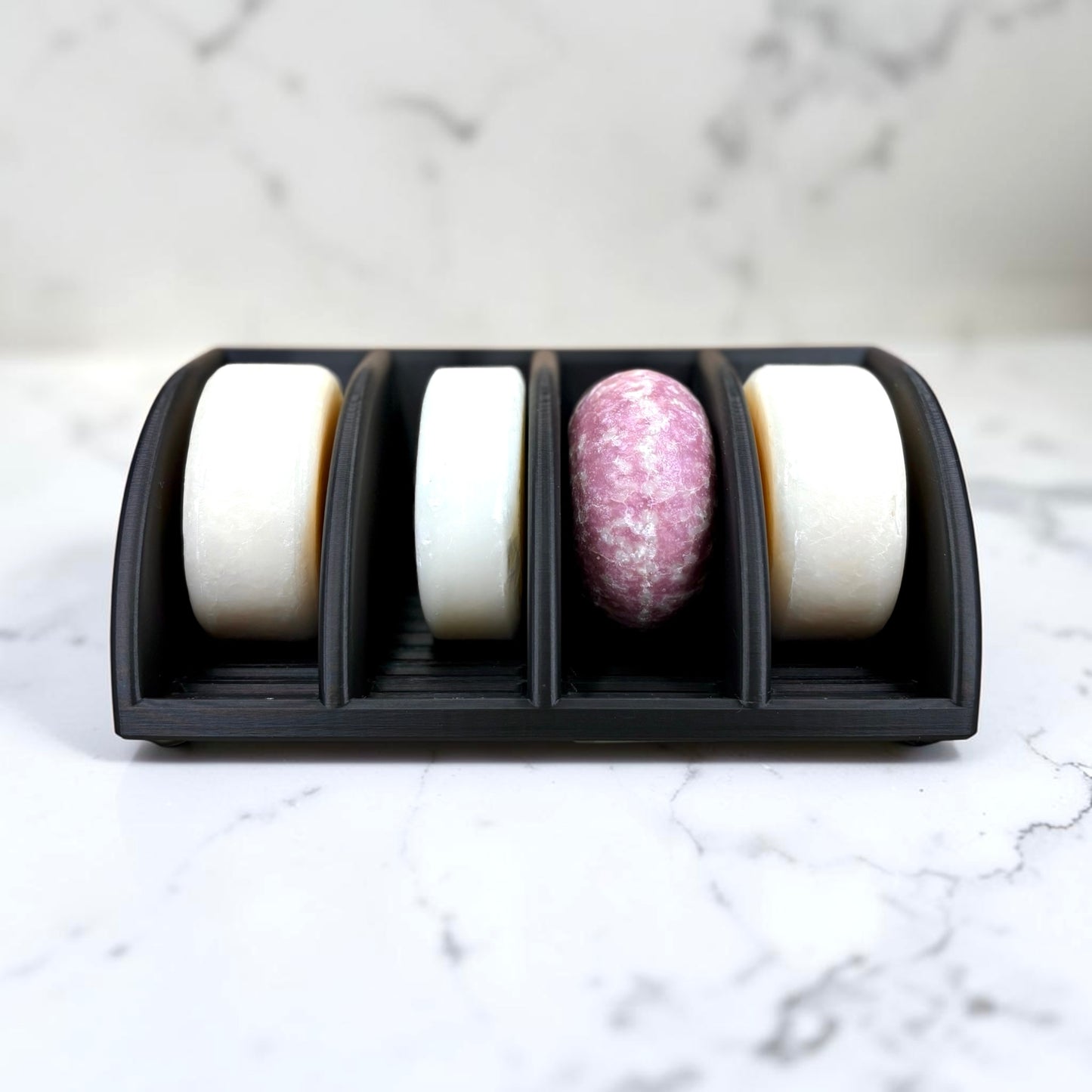 Four soap bars in a black holder on a marble surface