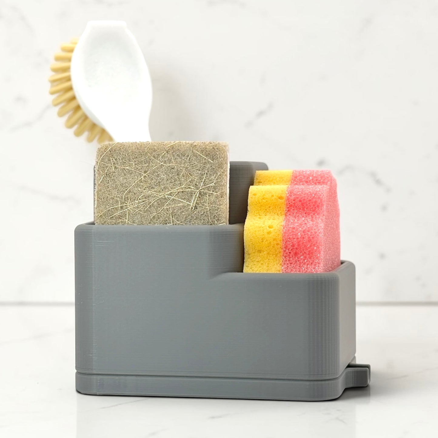 Gray sponge holder with sponges and a scrubber on a white surface.