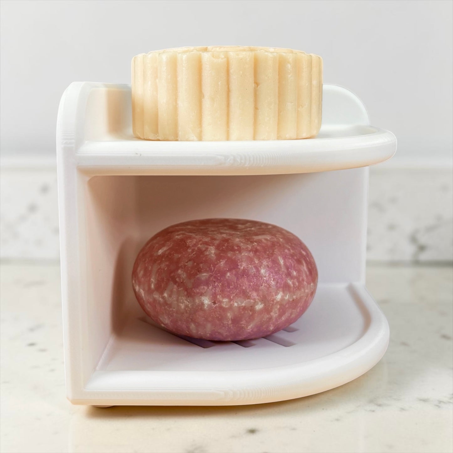 White soap holder with a two bars of soap on top on a marble counter