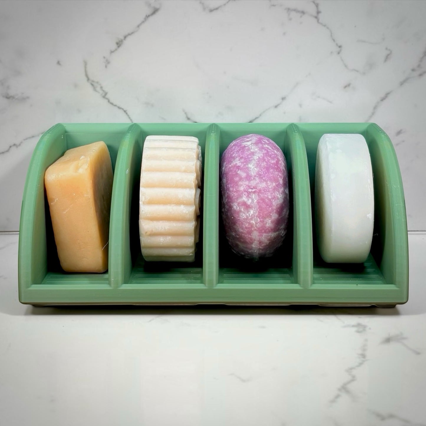 Four soaps in a green holder on a marble surface