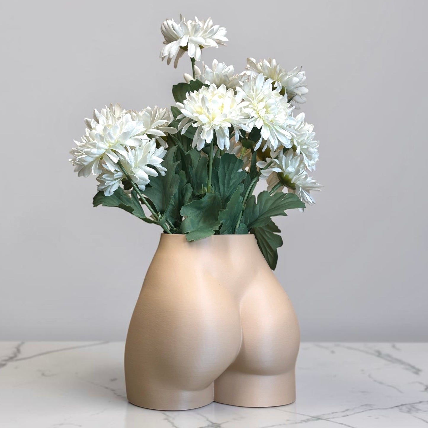 Light brown Vase shaped like a person's buttocks with white flowers on a marble surface