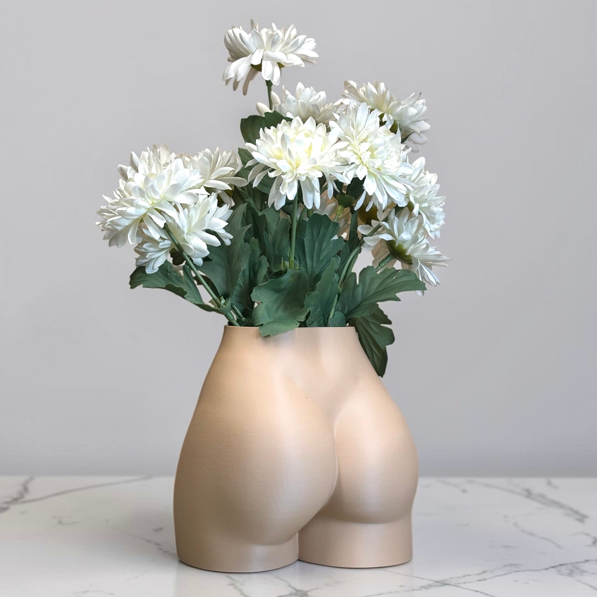 Light brown Vase shaped like a person's buttocks with white flowers on a marble surface