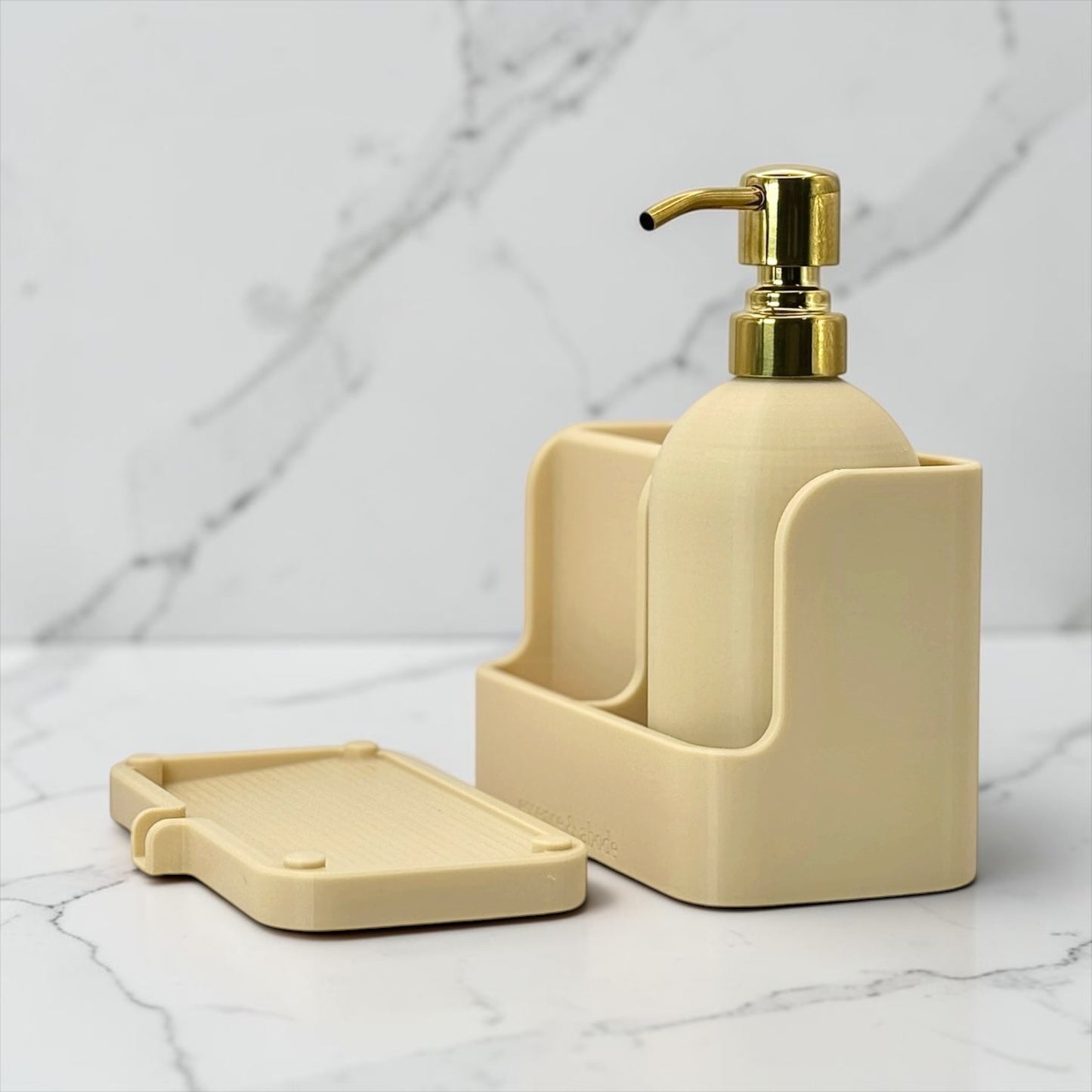 A cream-colored bathroom accessory set featuring a soap dispenser with a gold pump, a matching soap dish, and a soap holder, displayed on a white marble surface with a matching marble background.