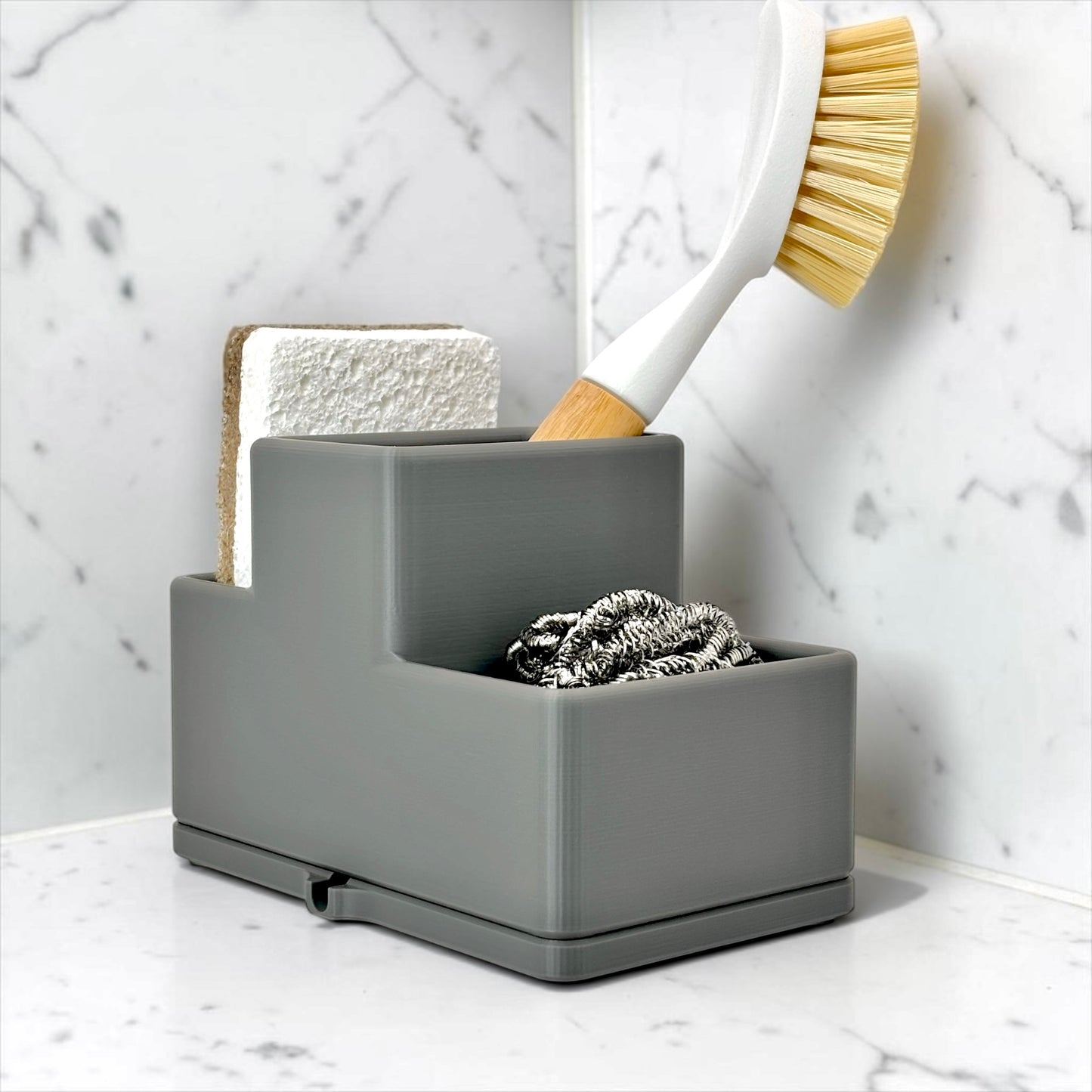 Gray cleaning caddy with sponge, brush, and scrubber on a marble countertop