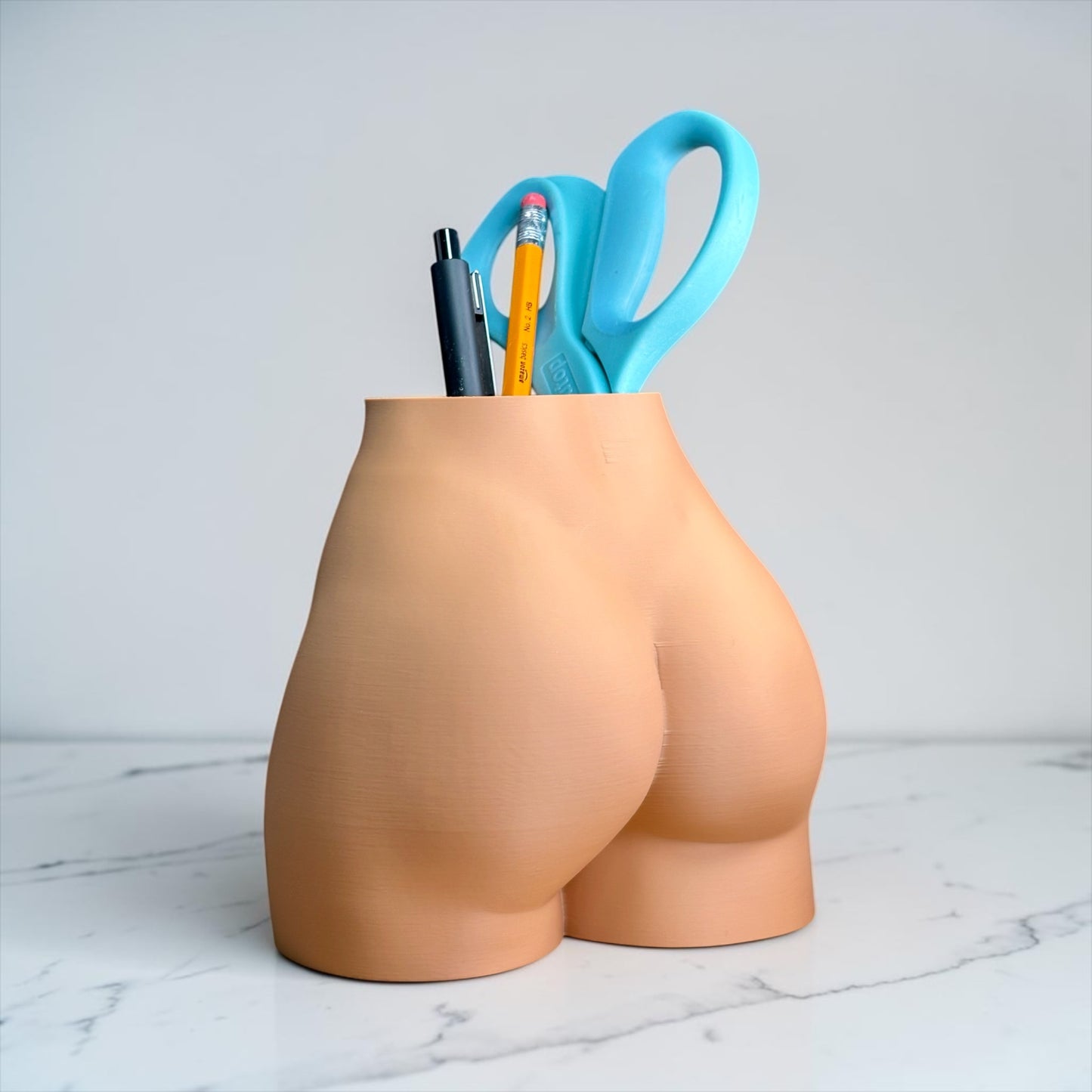 Vase shaped like a butt with office supplies on a marble surface