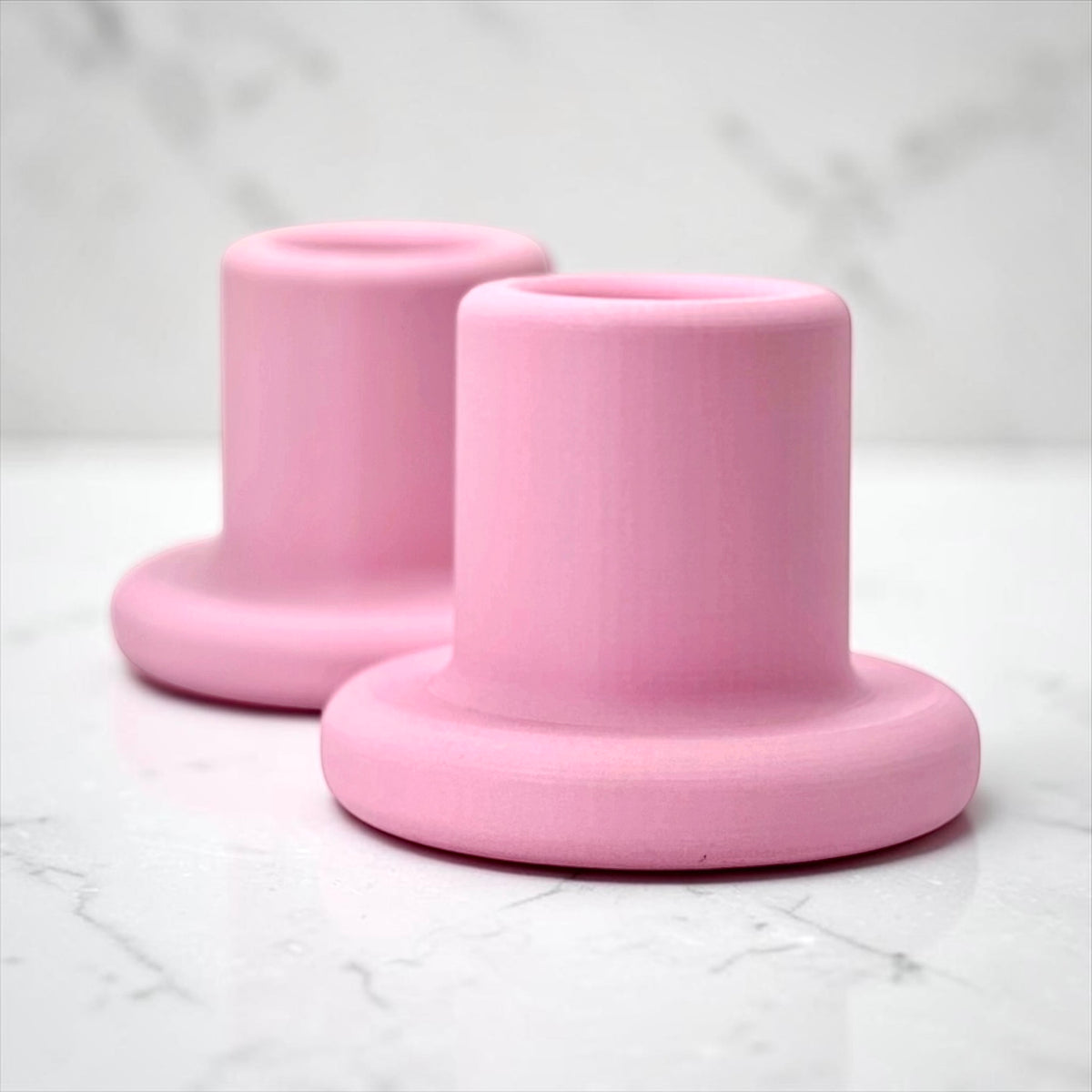 Two pink silicone cup holders with a flared base, arranged on a light marble surface with a matching marble background.