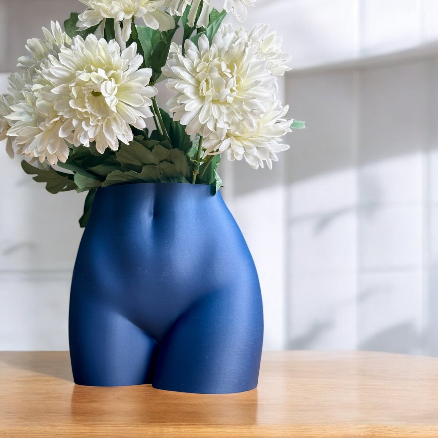 Blue vase shaped like a butt with white flowers on a wooden surface