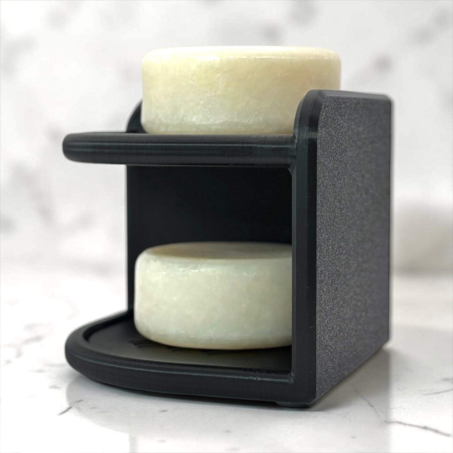 Black soap holder with two bars of soap on a marble surface