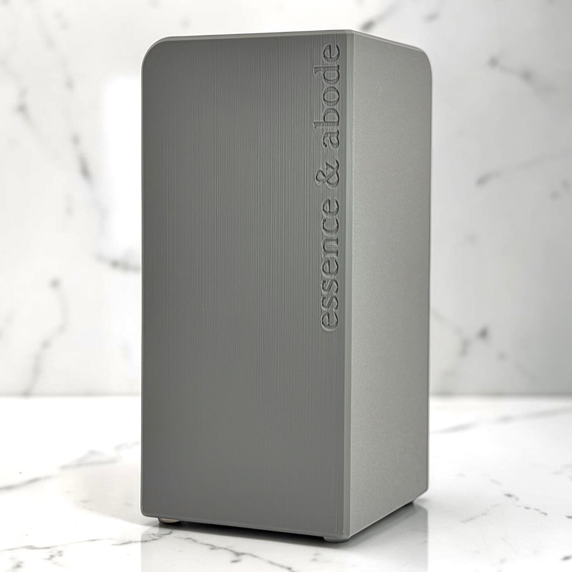 Gray container with 'essence & abode' branding on a marble surface