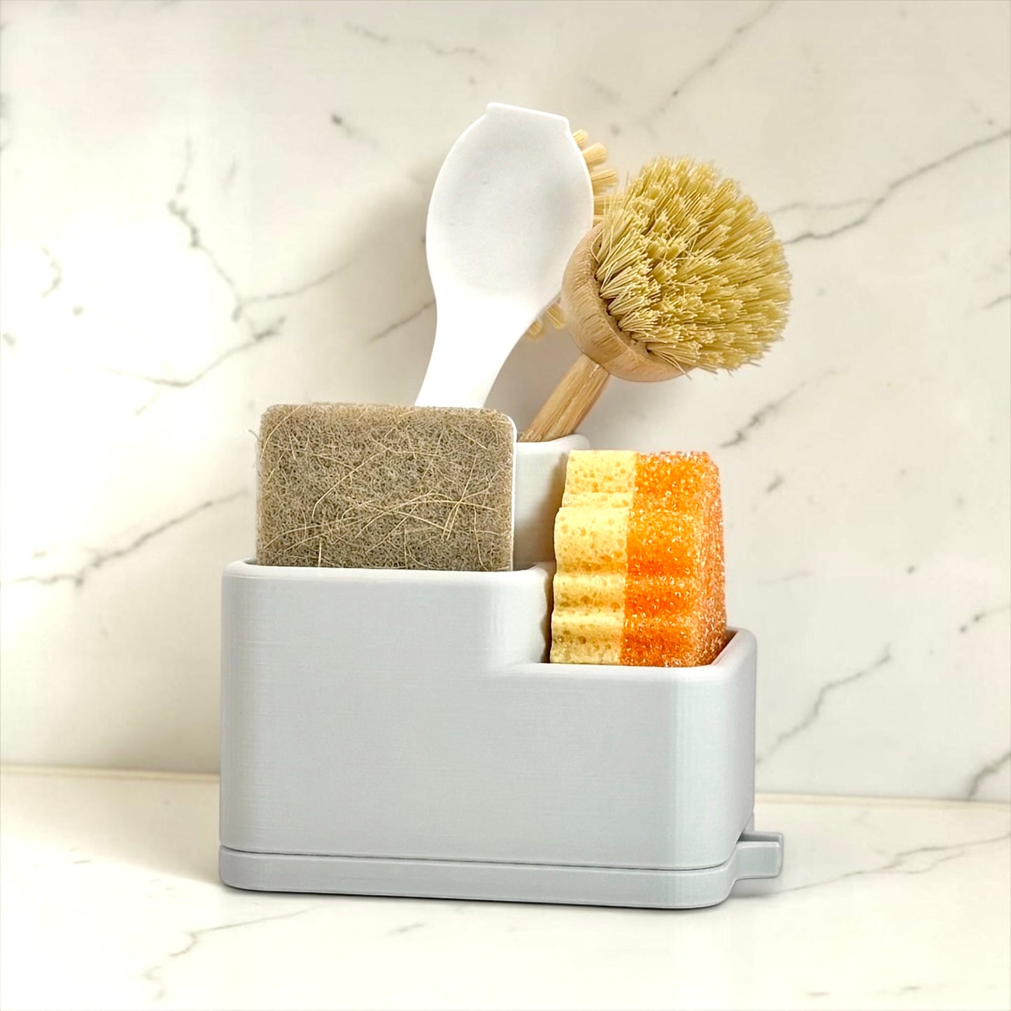 Set of cleaning tools including a brush, scrubber, and sponge in a holder on a marble background