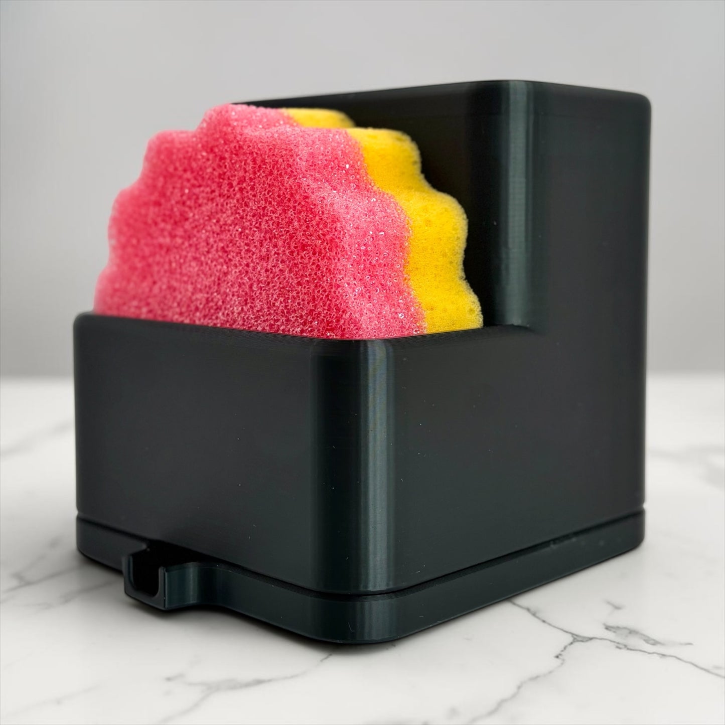 Black sponge holder with pink and yellow sponges on a marble surface