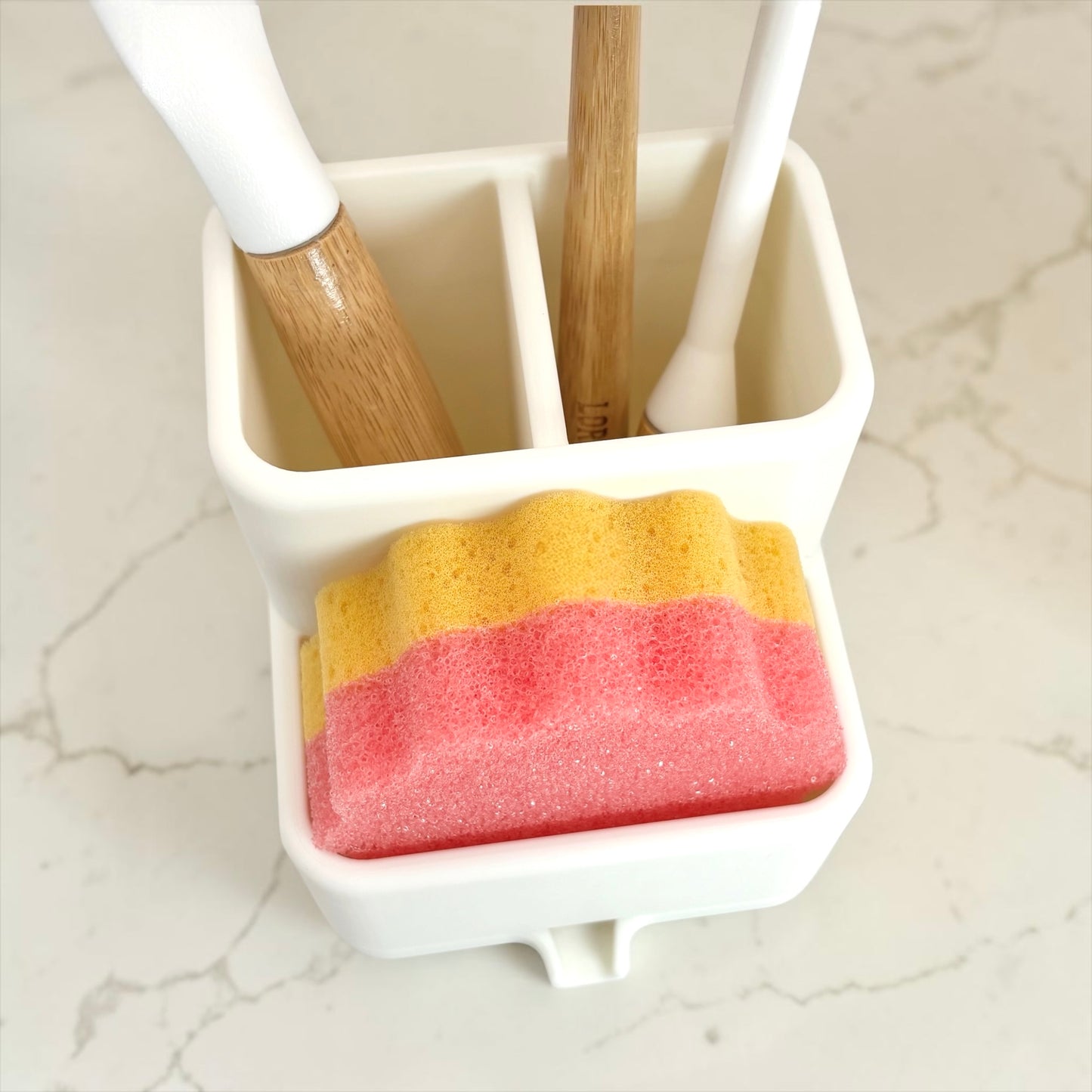 Cleaning tools including a brush, sponge, and scrubber in a holder on a marble surface.