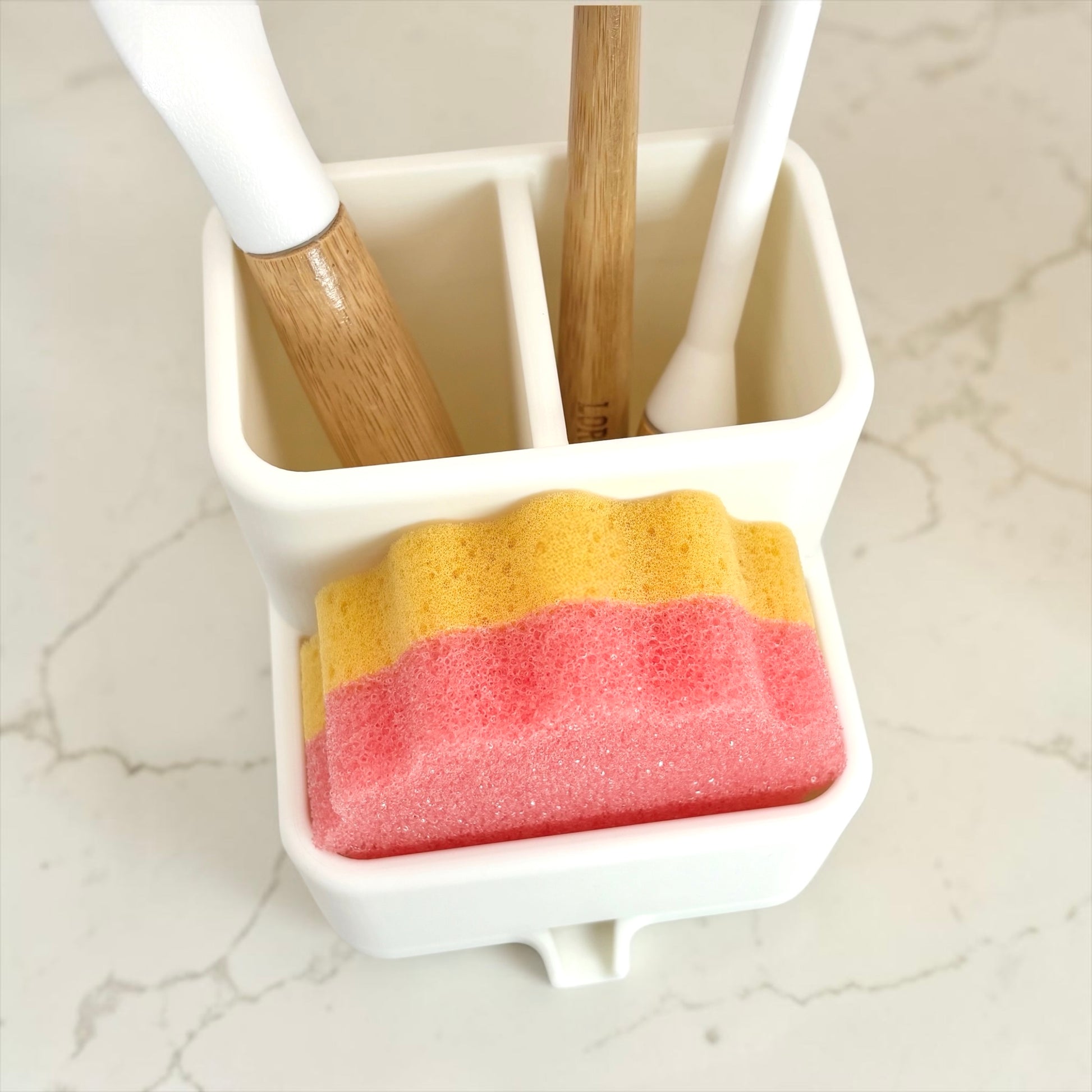 Cleaning tools including a brush, sponge, and scrubber in a holder on a marble surface.