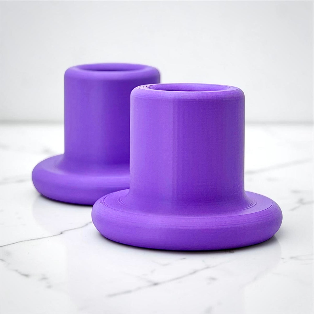 Two purple cylindrical holder stands with flared bases, shown on a white marble surface against a light gray background.