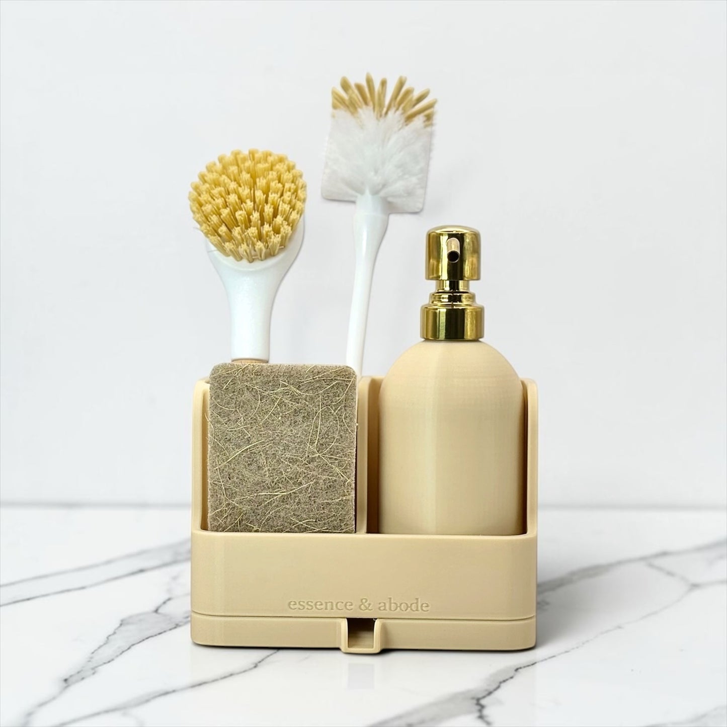 A beige bathroom organizer set on a white marble surface, featuring a pump bottle with a gold cap, a sponge, a brush with yellow bristles, and a scrubber.