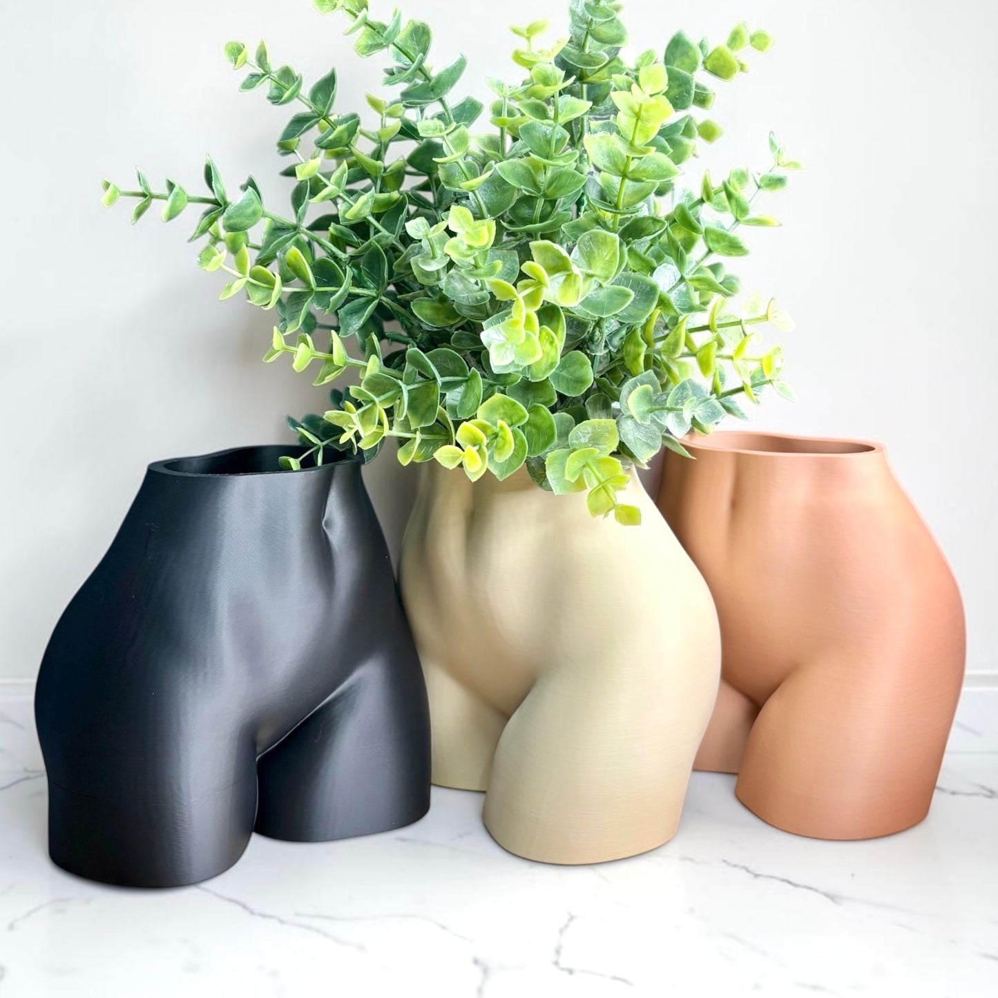 Three curvy vases shaped like a butt with plants on a light background