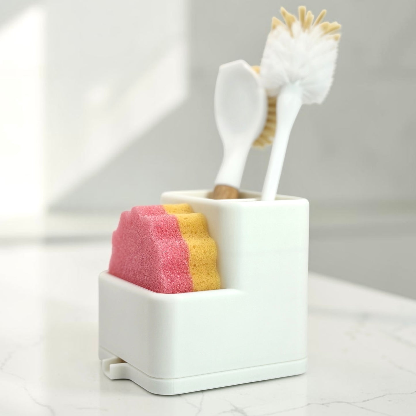 White utensil holder with a dish brushes, and two colorful sponges on a light gray background.