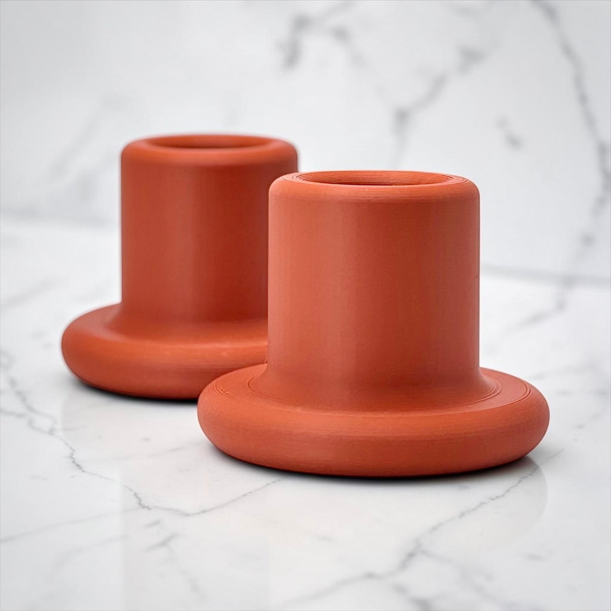Two terracotta-colored silicone cup holders with a matte finish, displayed on a white marble surface.