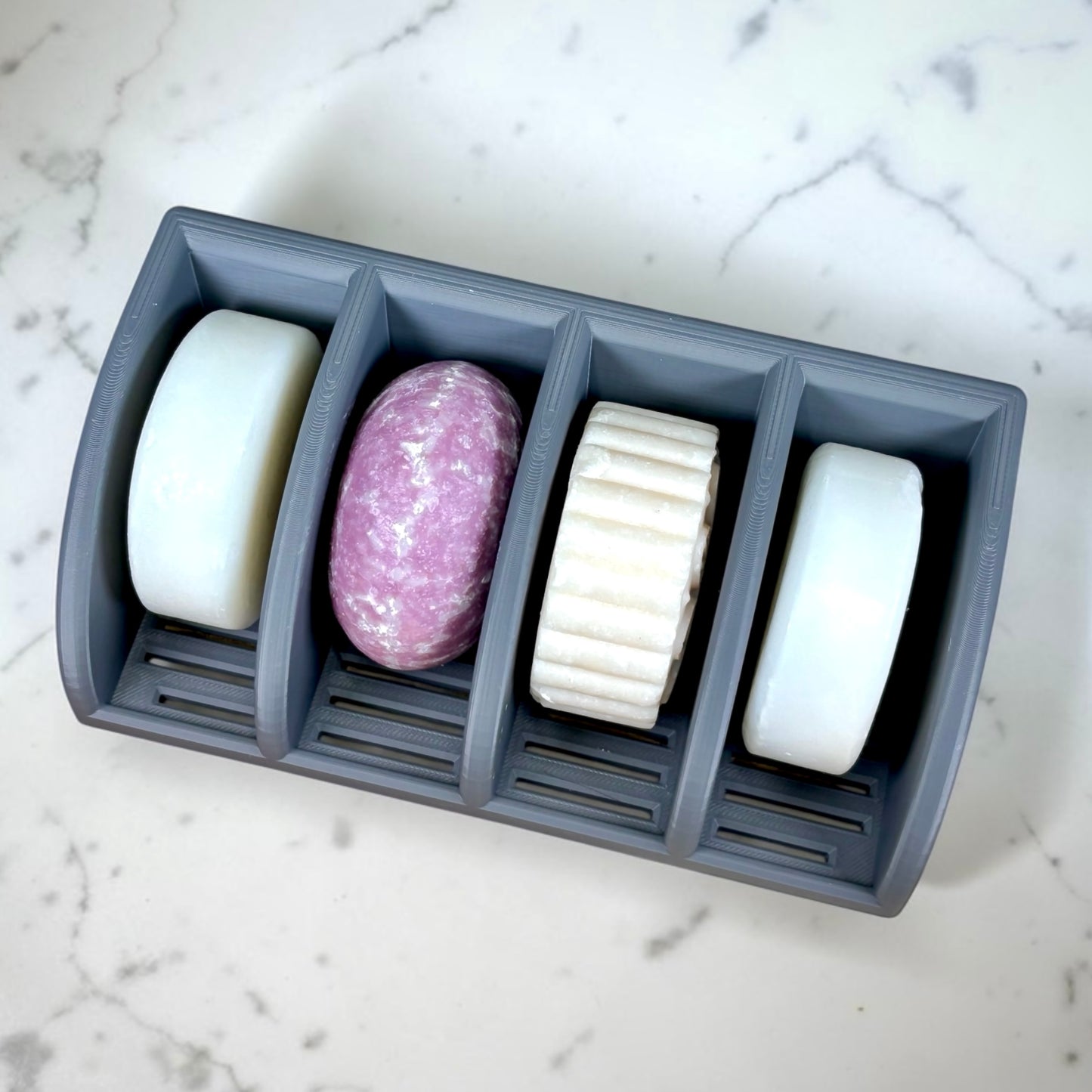 Gray soap holder with four bars of soap on a marble surface