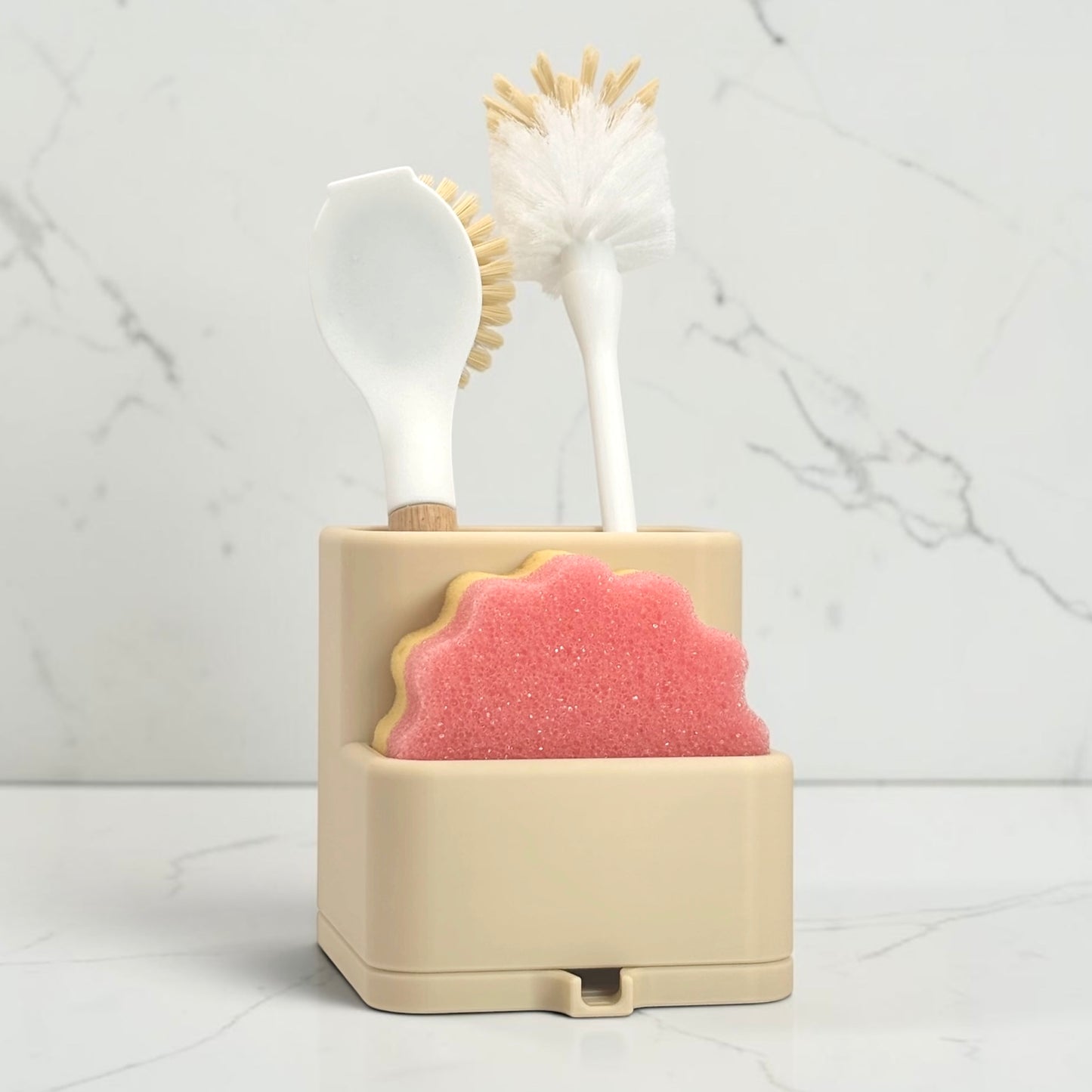 Beige dishwashing brush holder with a pink sponge and white scrubber on a marble background