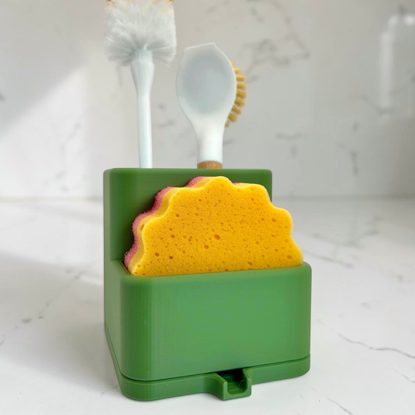 Green holder with a yellow sponge and white scrubber on a light gray background