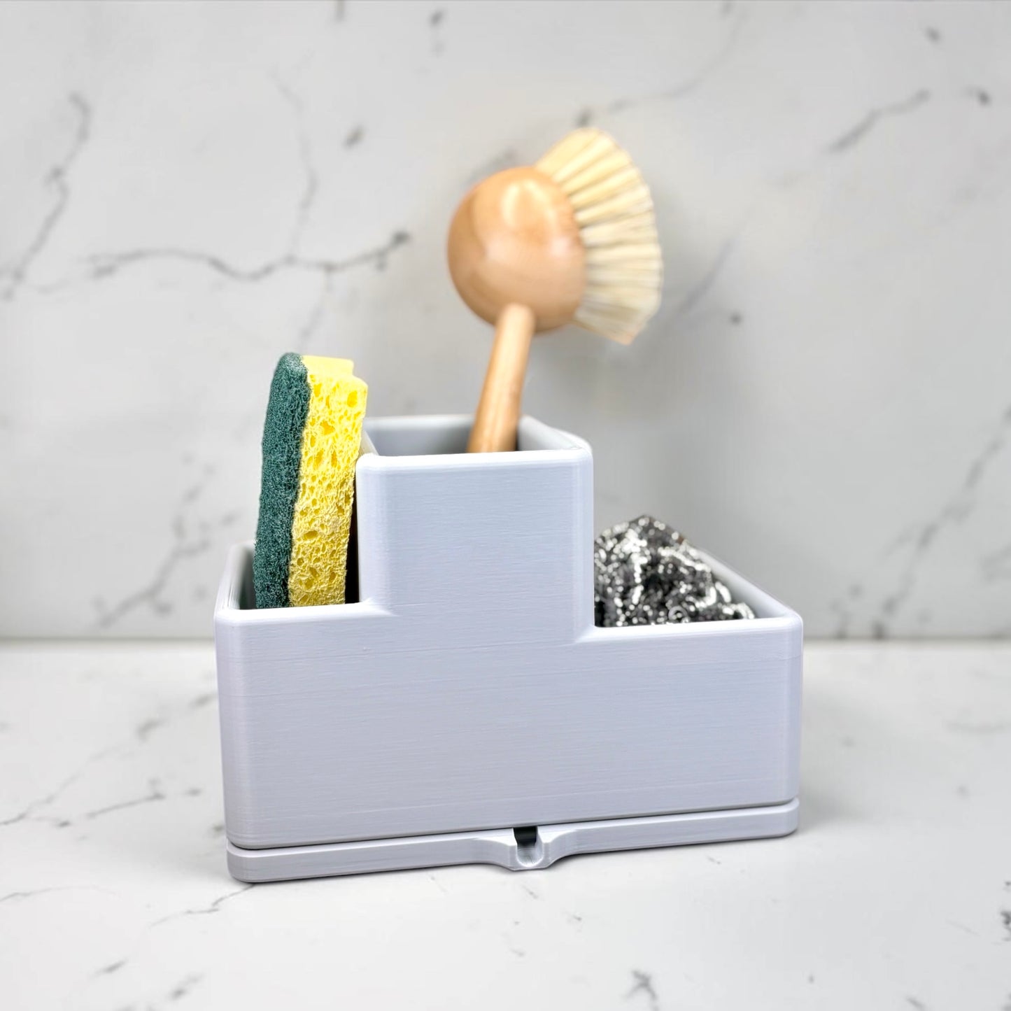 Gray caddy with sponge, brush, and scrubber on a marble countertop