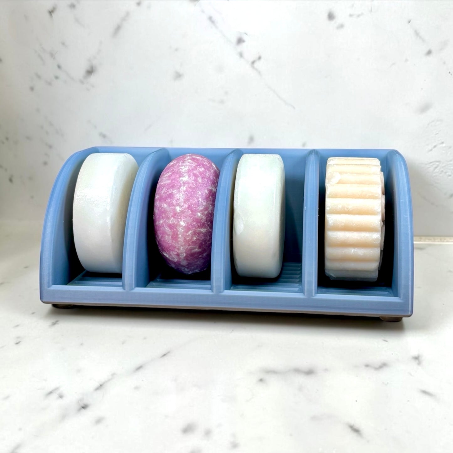 Four soap bars in a blue holder on a marble surface