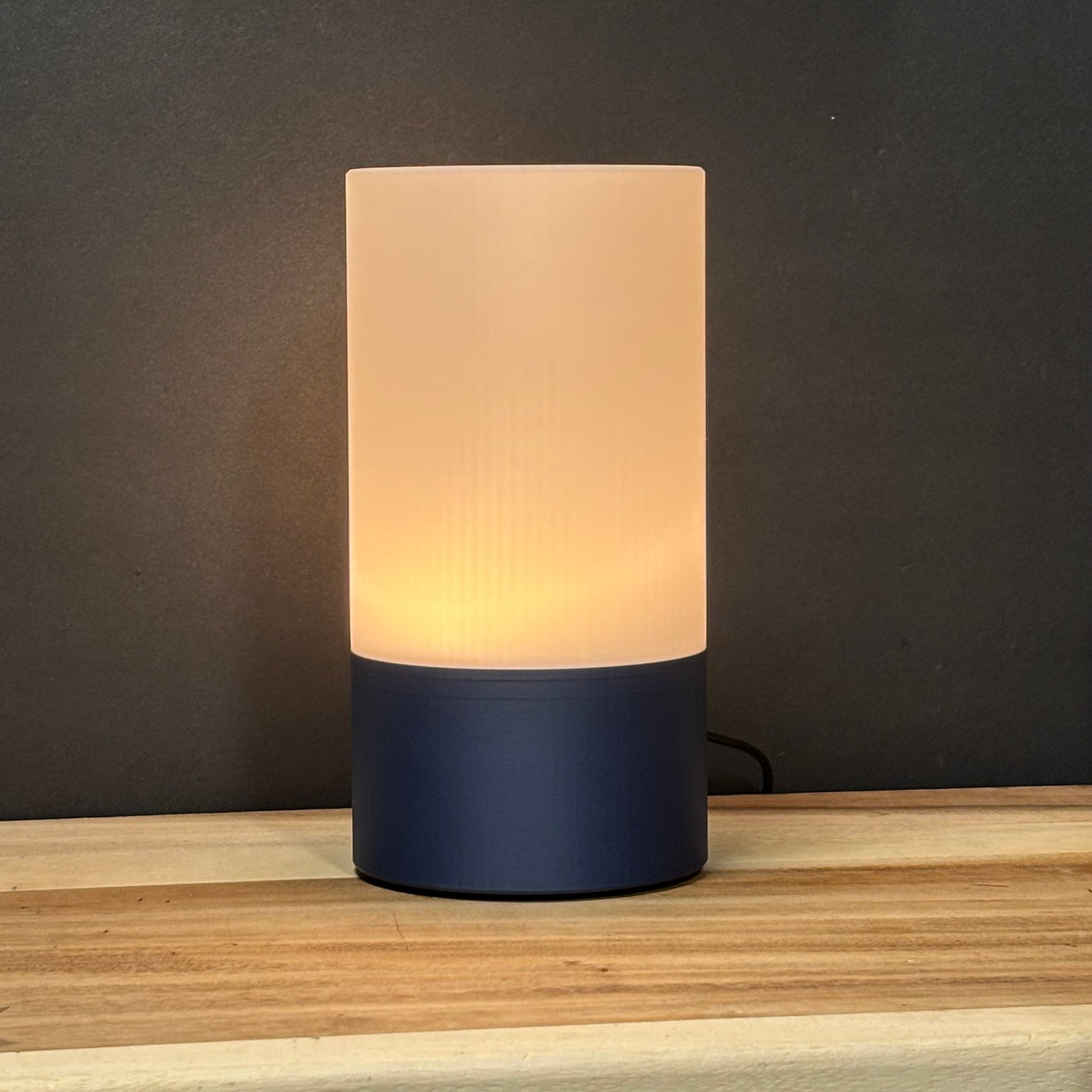 Table lamp with a beige glass shade and navy base on a wooden surface.