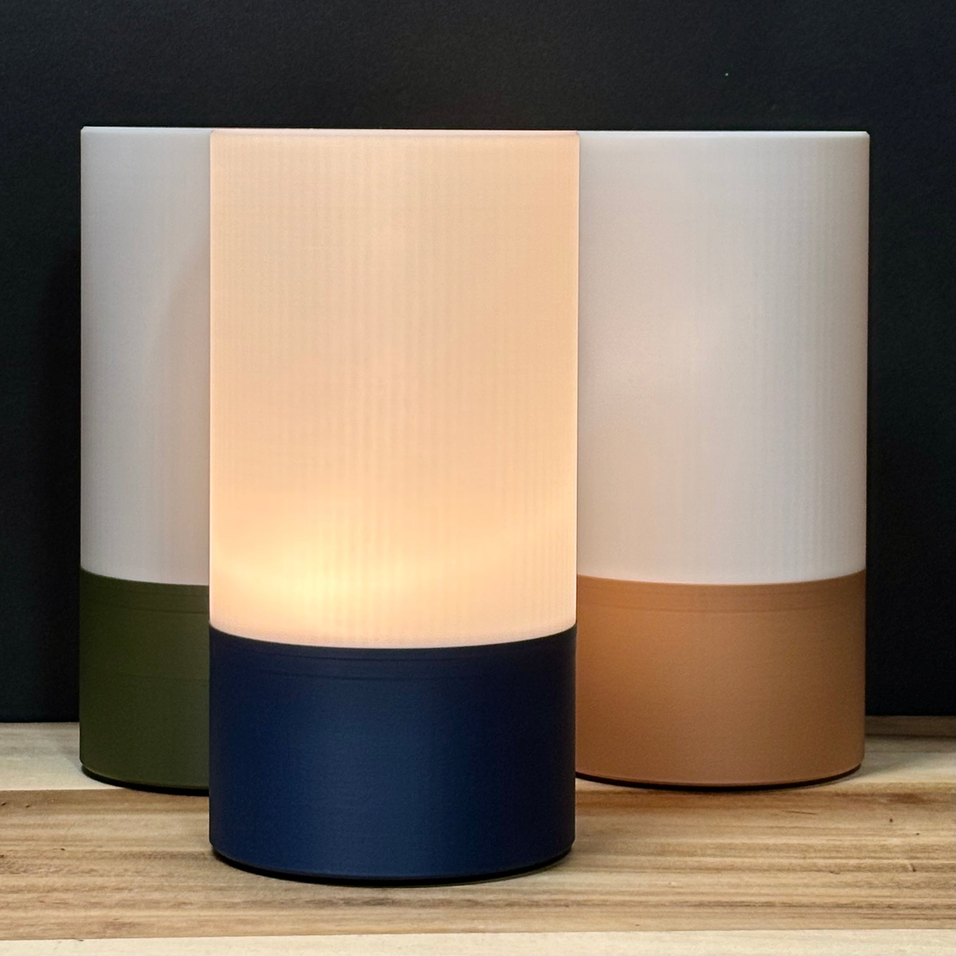 Three cylindrical lamps with different color combinations on a wooden surface.
