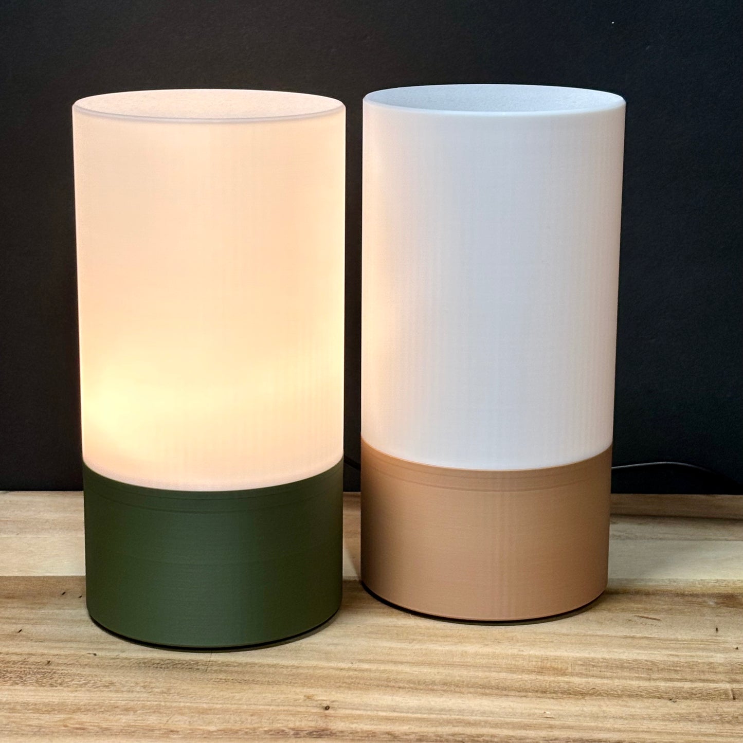Two cylindrical lamps with different colored bases on a wooden surface.