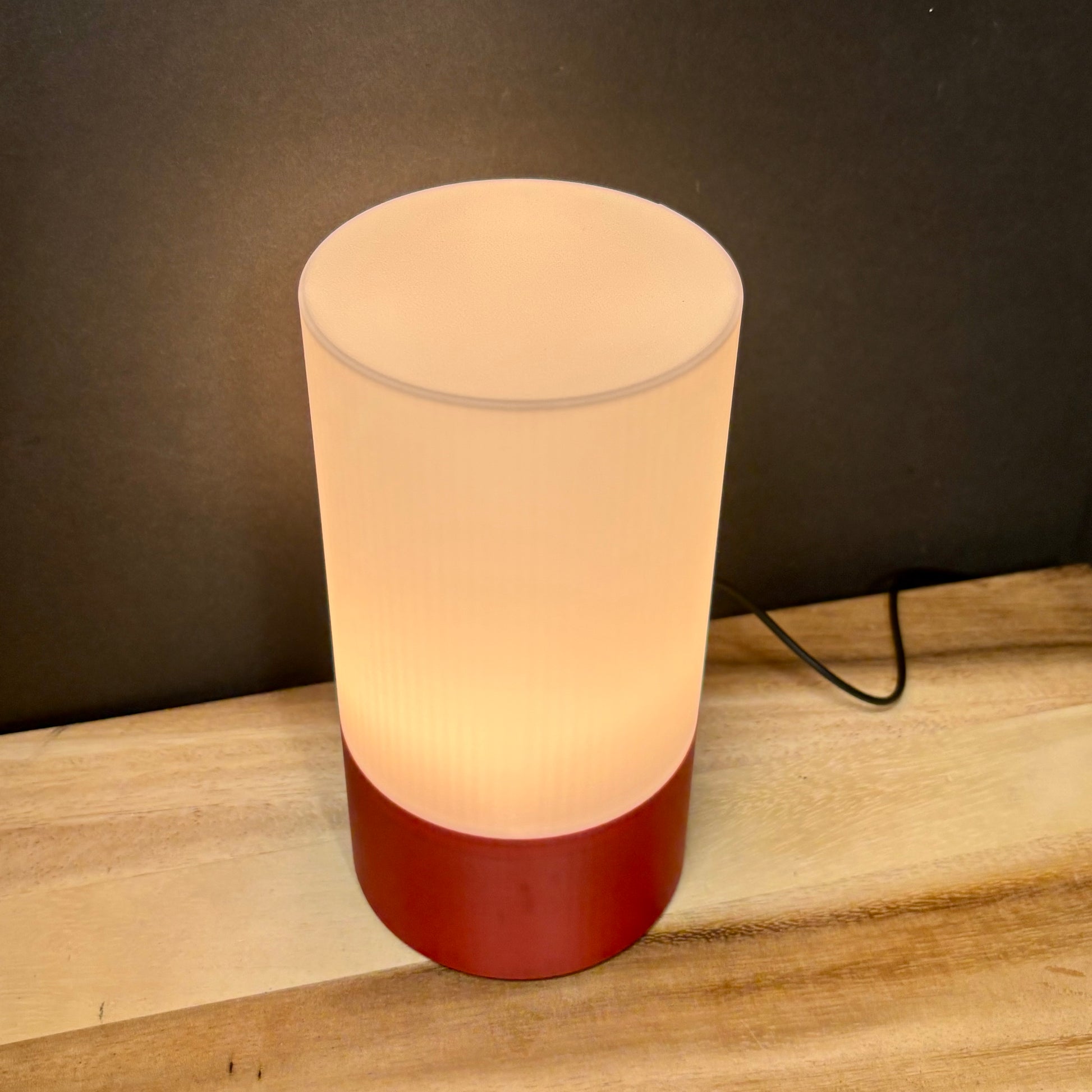 Cylindrical lamp with a red base on a wooden surface against a dark background