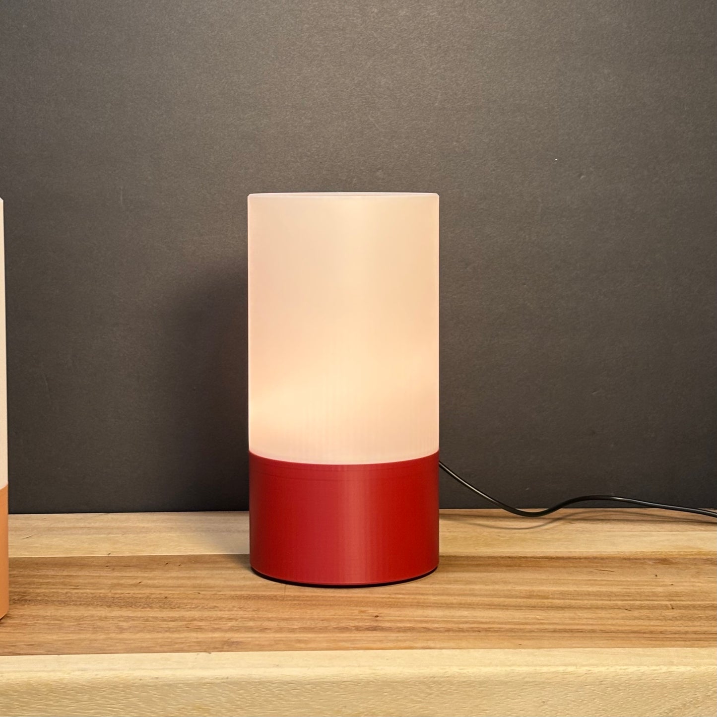 Cylindrical table lamp with a red base and white shade on a wooden surface.