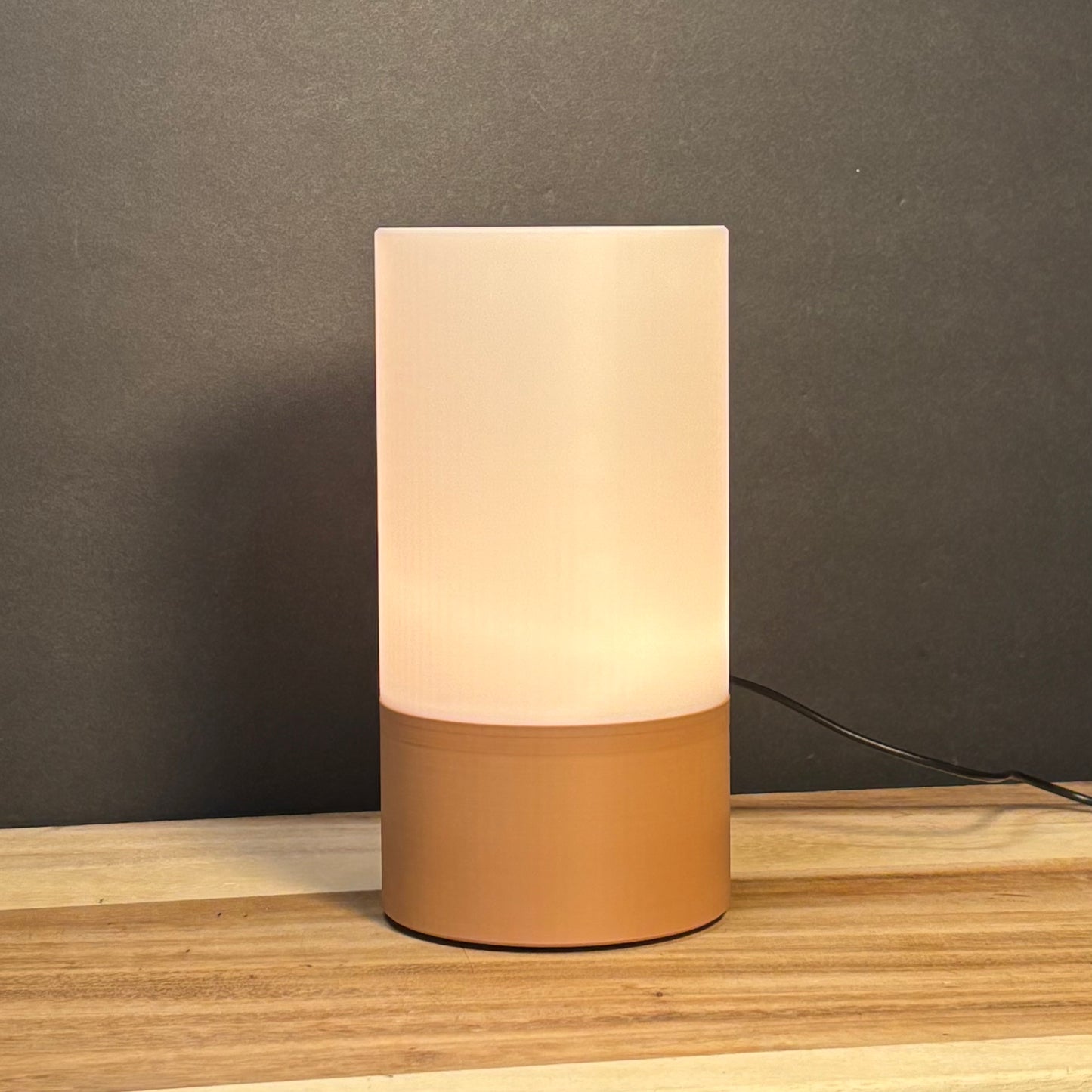 Table lamp with beige cylindrical shade and base on a wooden surface with a dark background