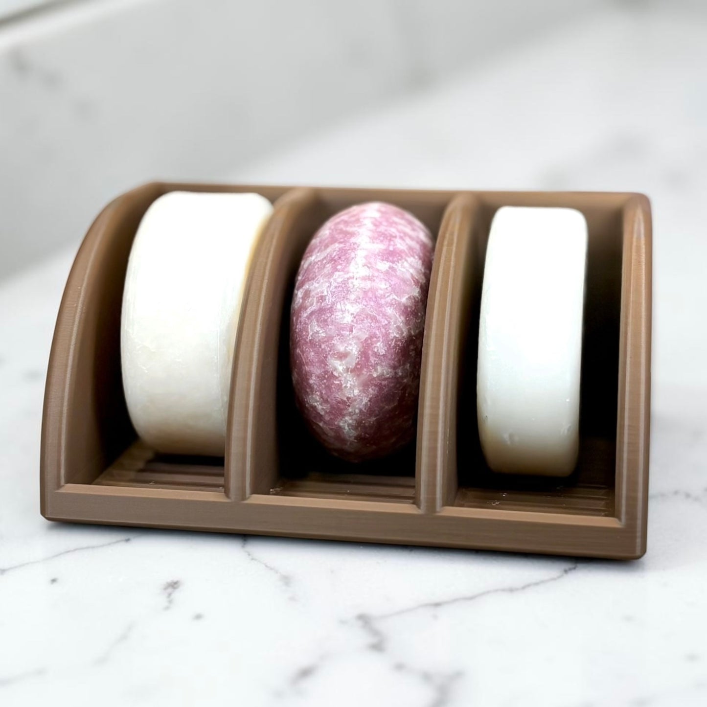 Three soap bars in a brown holder on a marble surface