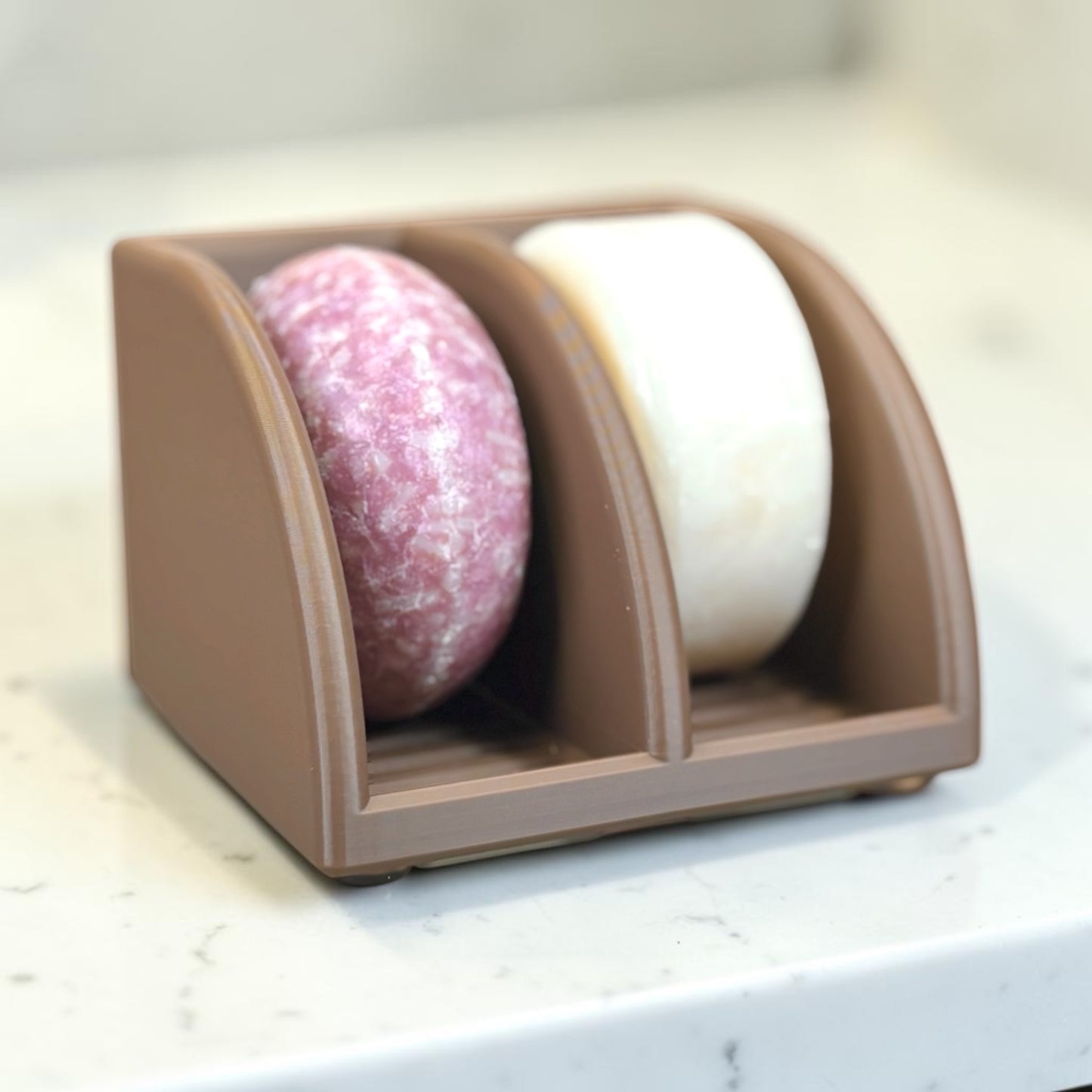 Two soap bars in a cocoa brown holder on a light surface