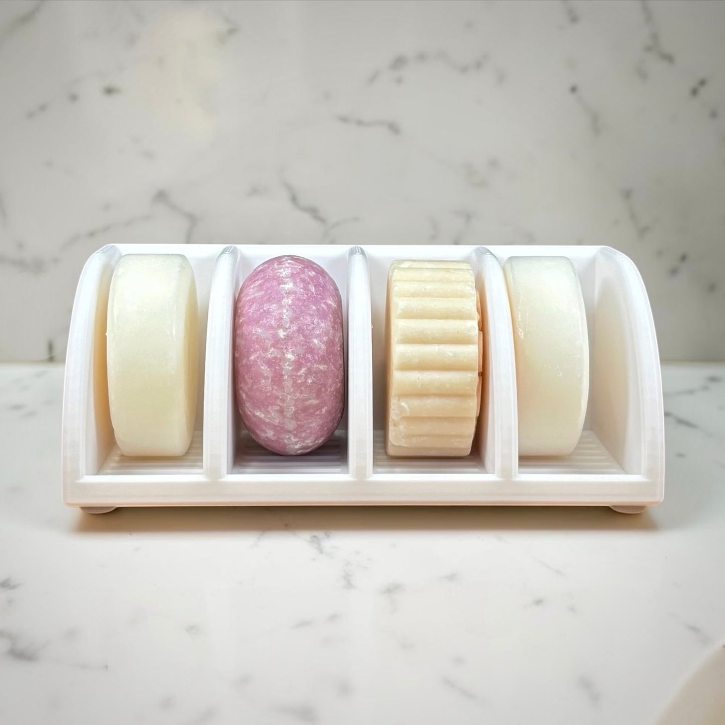Set of four soaps in a white holder on a marble surface