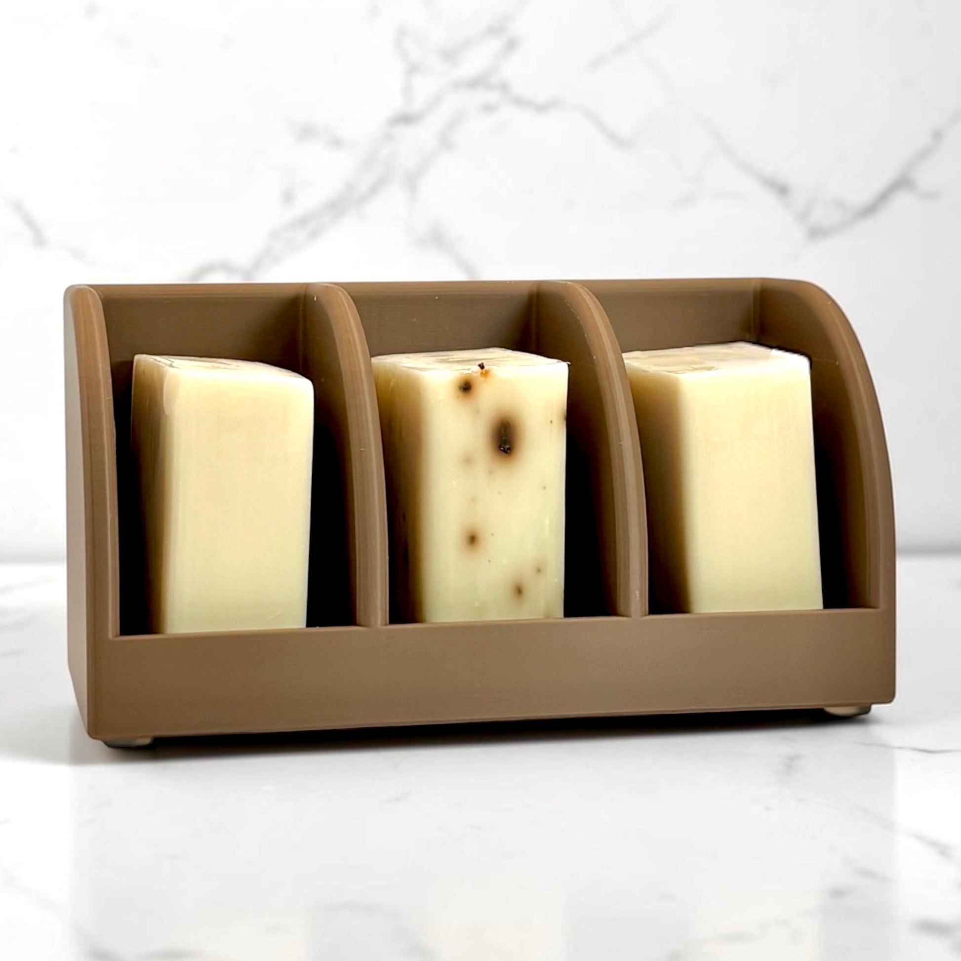 Brown soap holder with three bars of soap on a marble surface