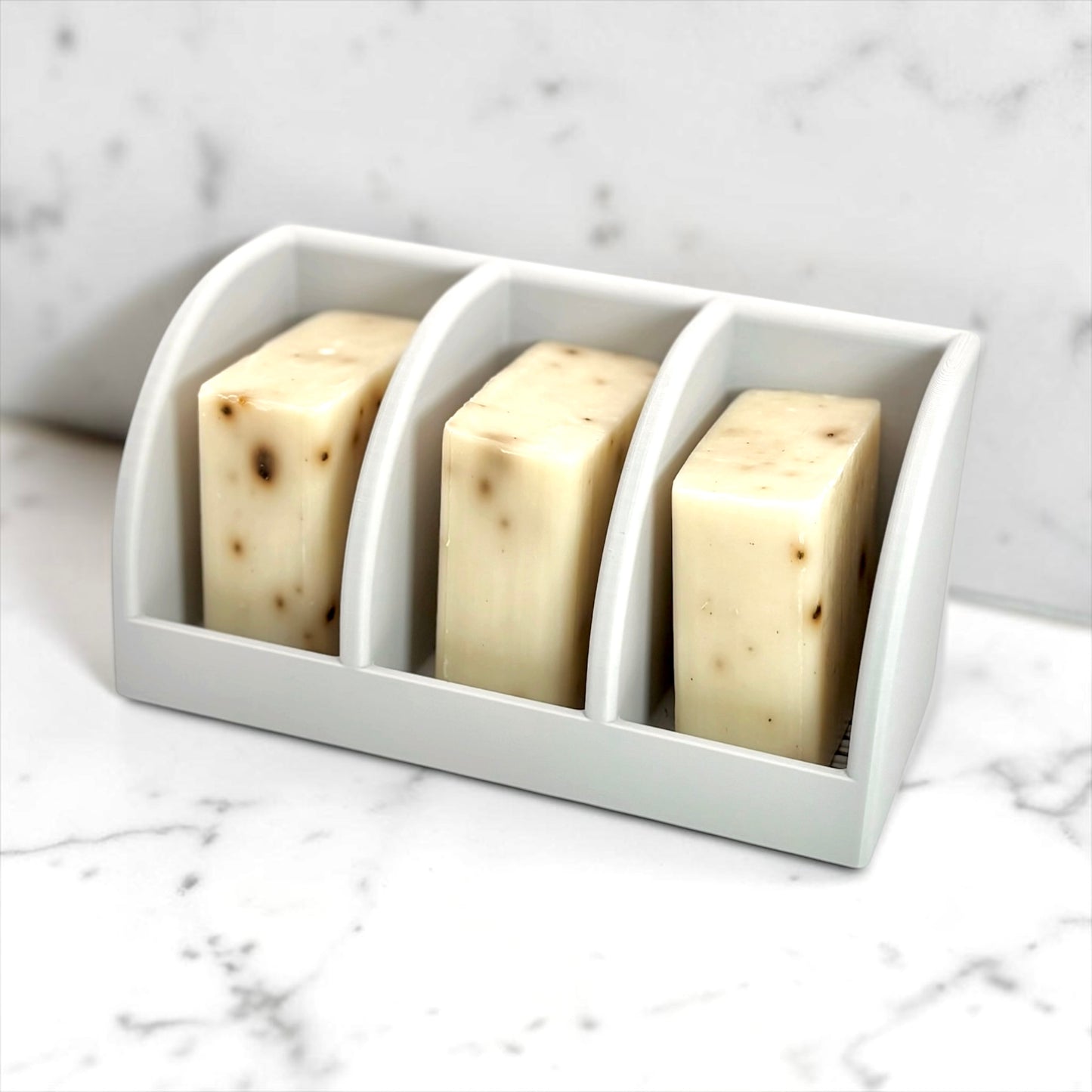 Three bars of soap in a white holder on a marble surface