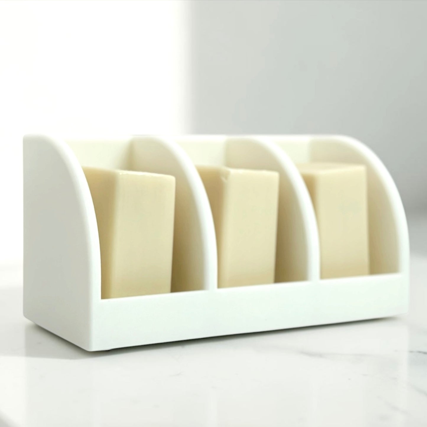 White soap holder with three bars of soap on a white background