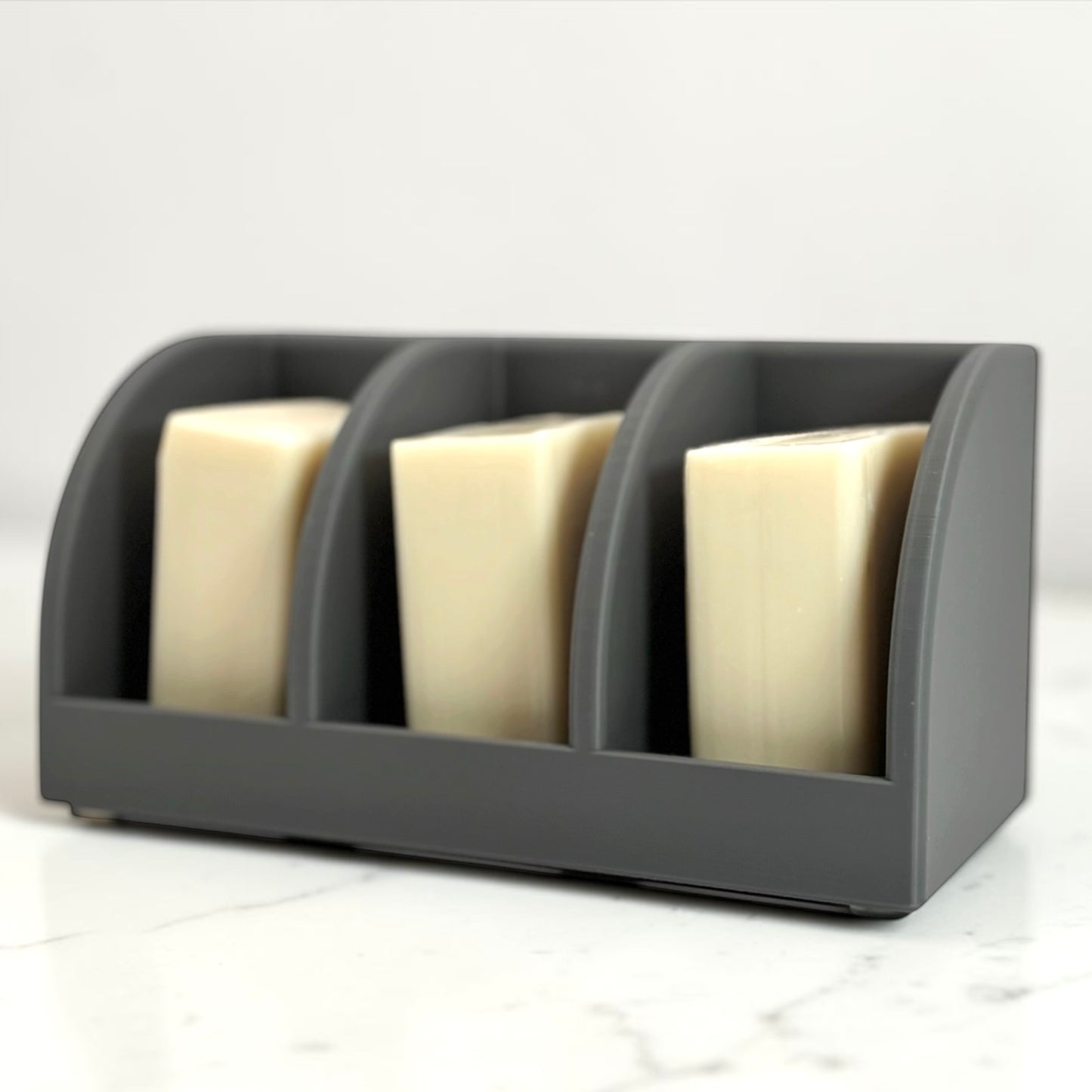 Gray soap holder with three bars of soap on a white marble surface