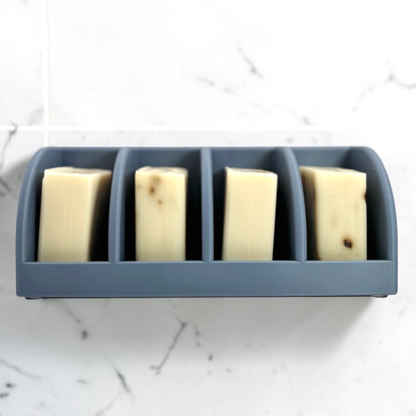 misty blue soap holder with four bars of soap attached to a marble wall