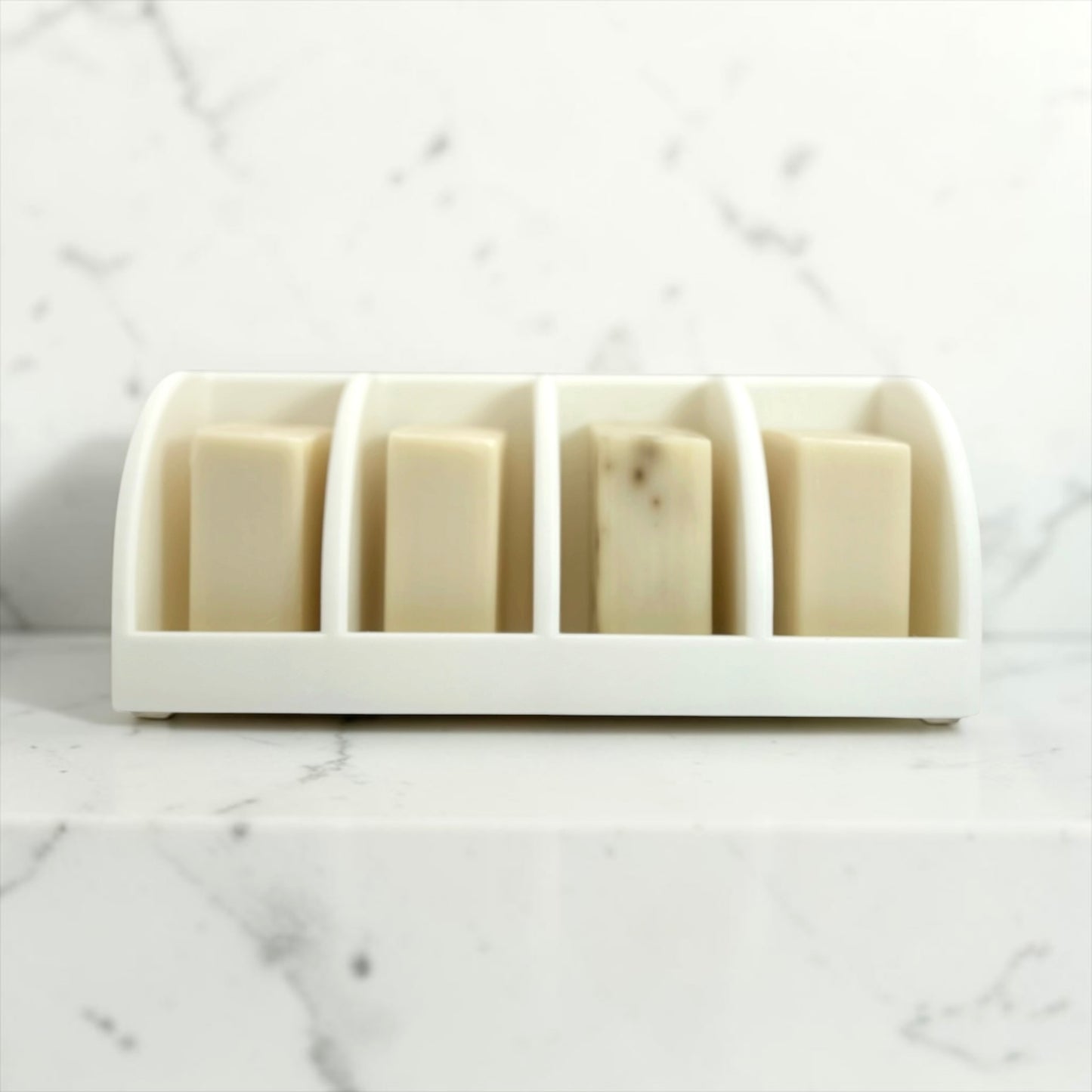 White soap holder with four bars of soap on a marble surface