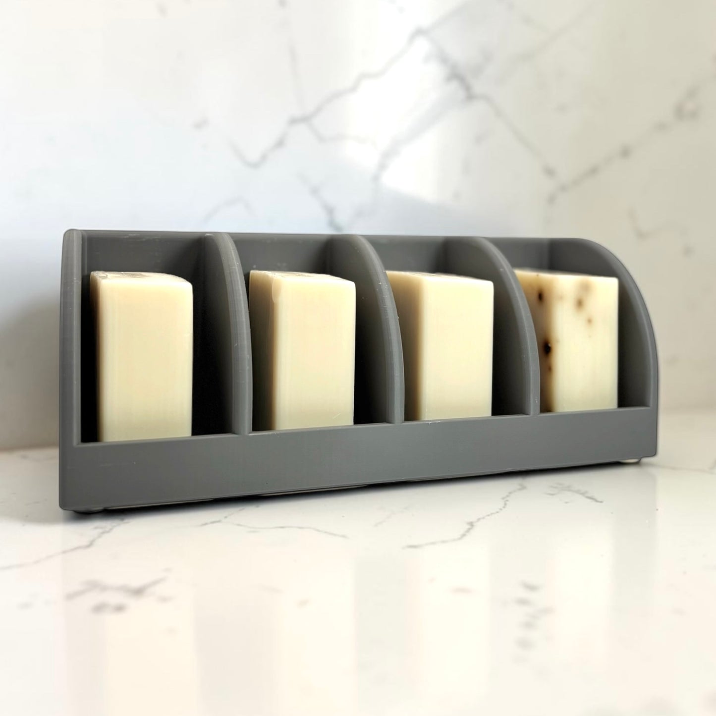 dark gray soap holder with four bars of soap on a marble countertop