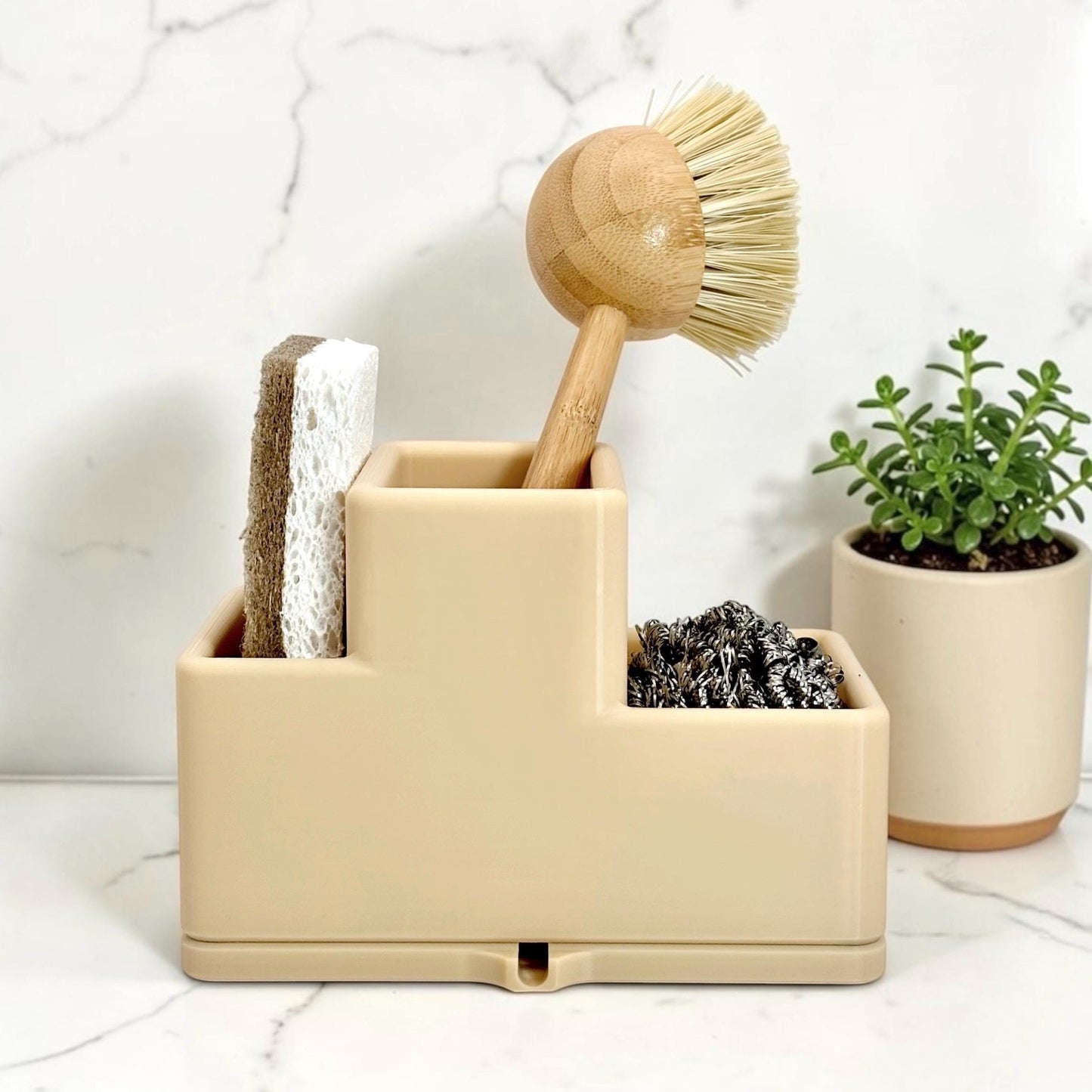 Beige caddy with cleaning tools including a brush, sponge, and scrubber on a marble surface.