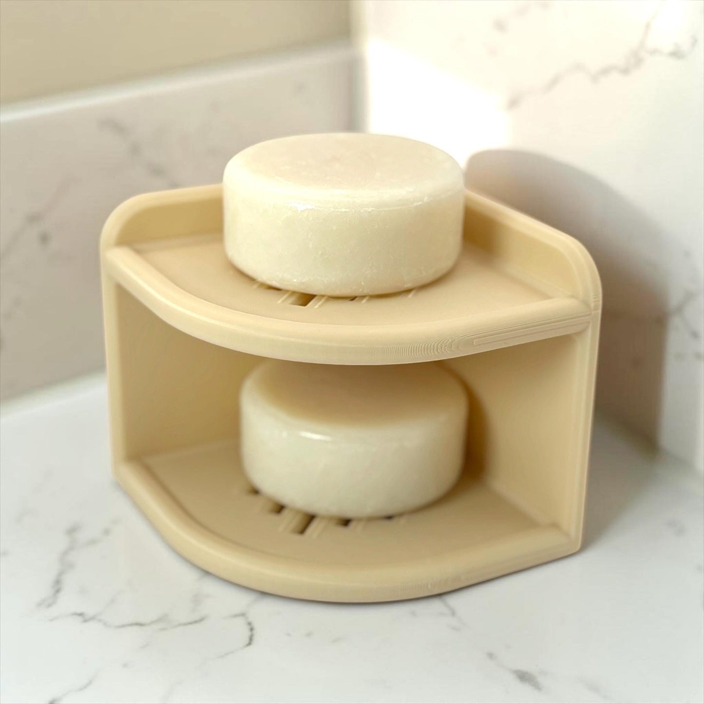 Beige corner soap holder with two bars of soap on a marble surface.