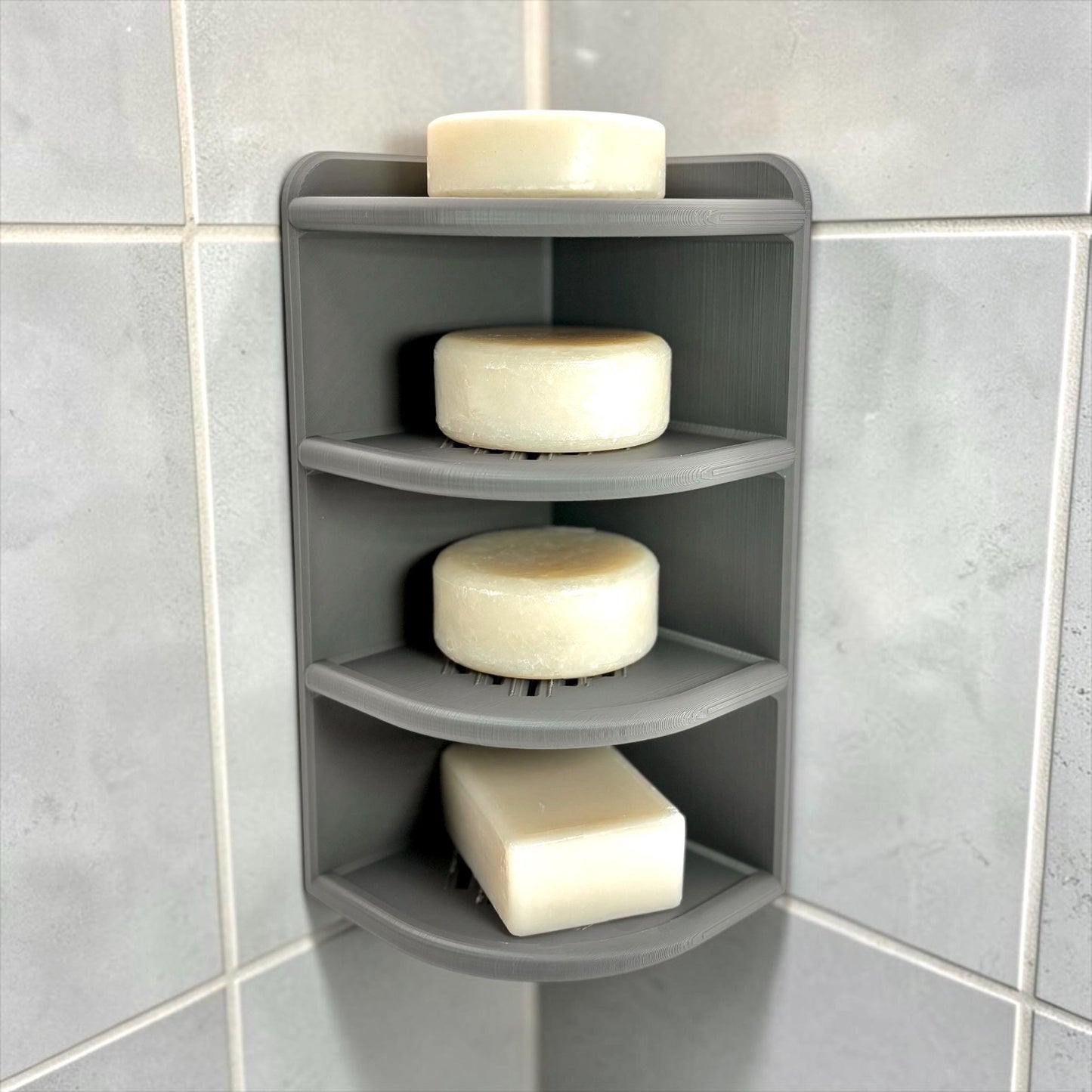 Gray corner shelf with soap bars on a tiled bathroom wall