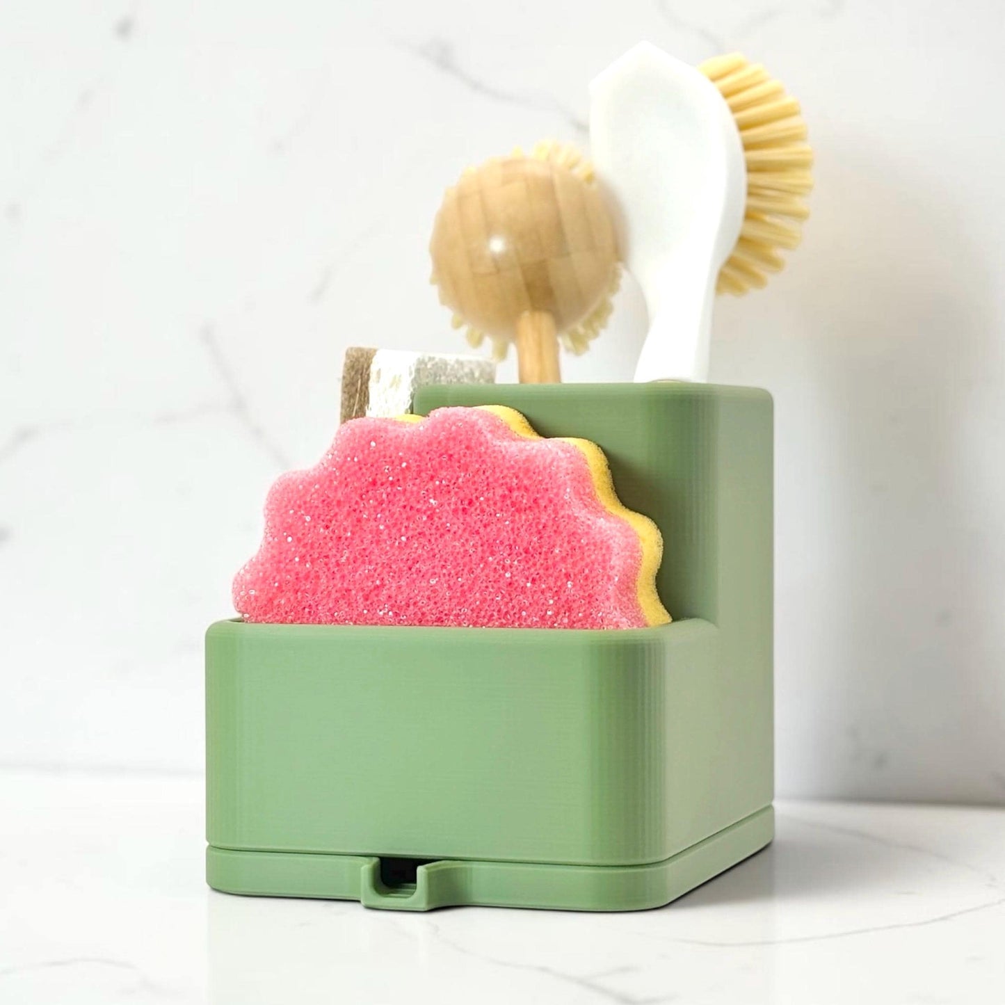 Green sponge holder with pink sponge, brush, and scrubber on a white background