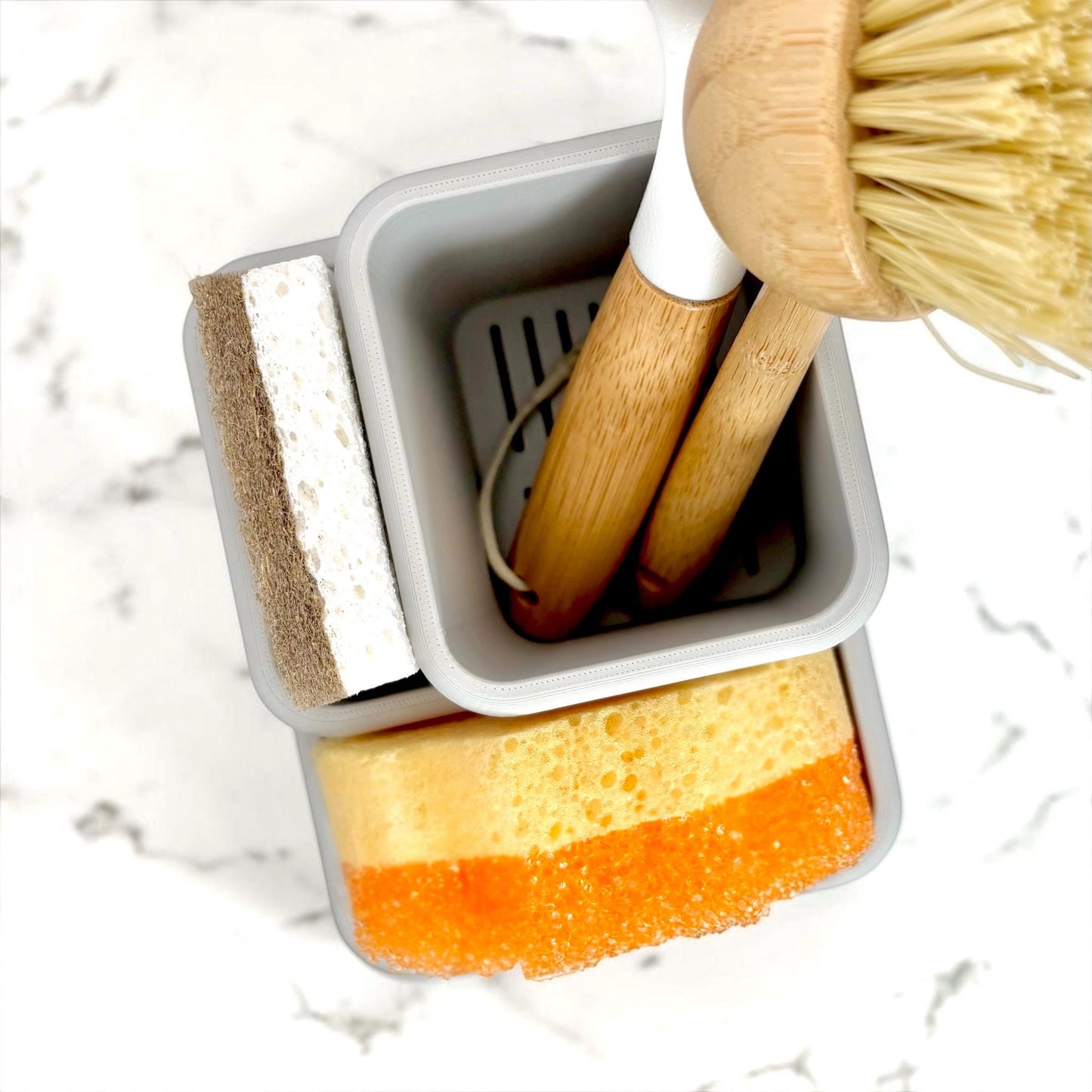 Set of cleaning tools including a scrubber, sponge, and brush in a holder on a marble surface.