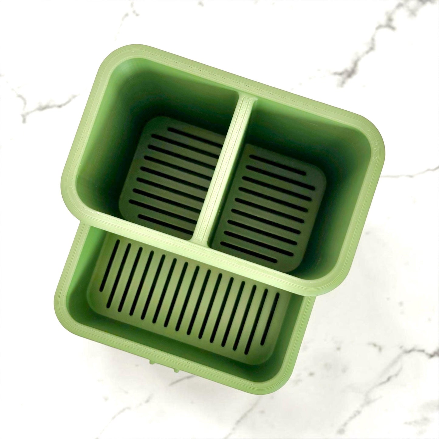 Green sink caddy viewed from above with divided compartments on a white marble background